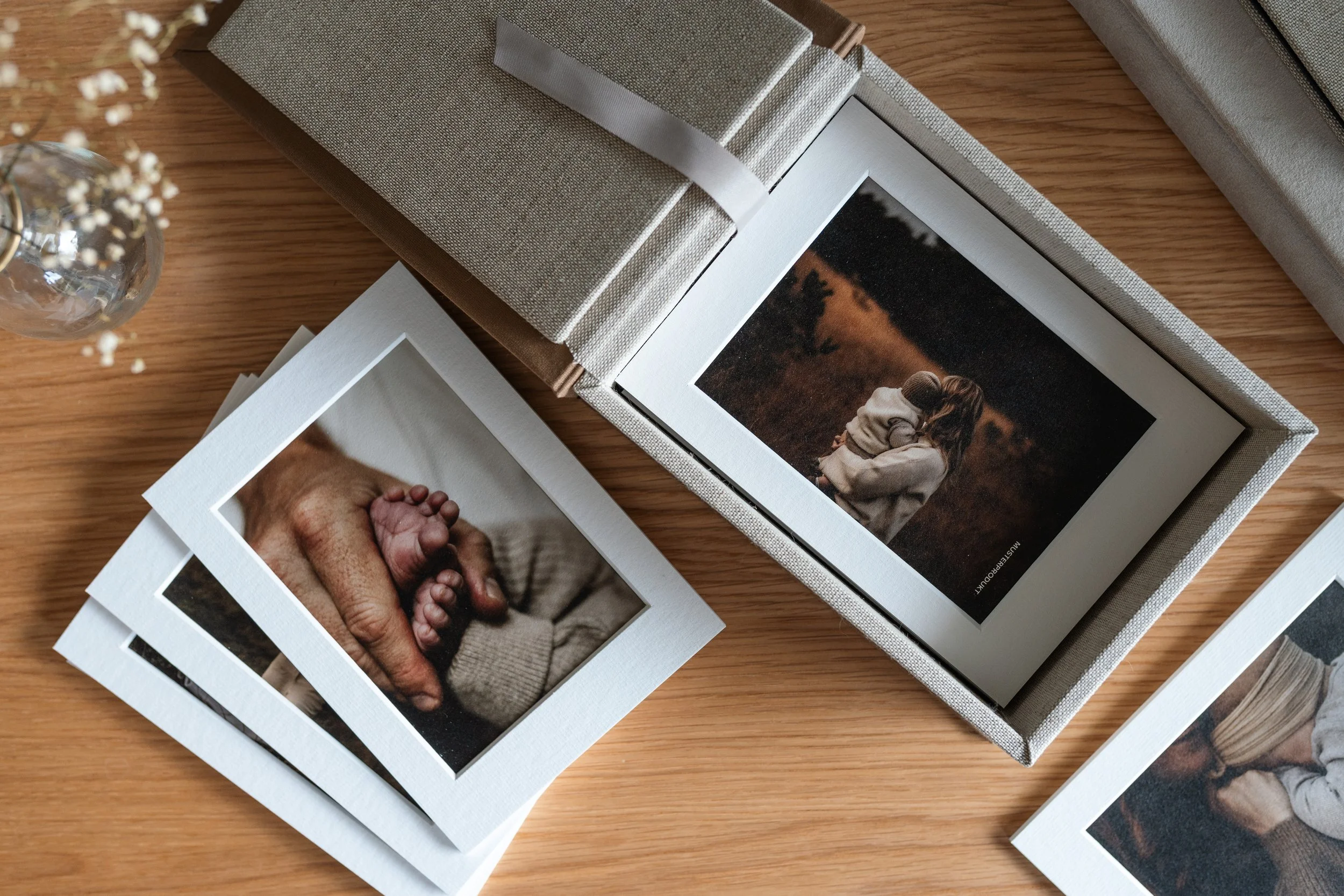 Fotobuch mit Fotos von einer Hand, die ein Baby hält, und einer Frau, die ein Kind im Park umarmt, auf einem Holztisch.