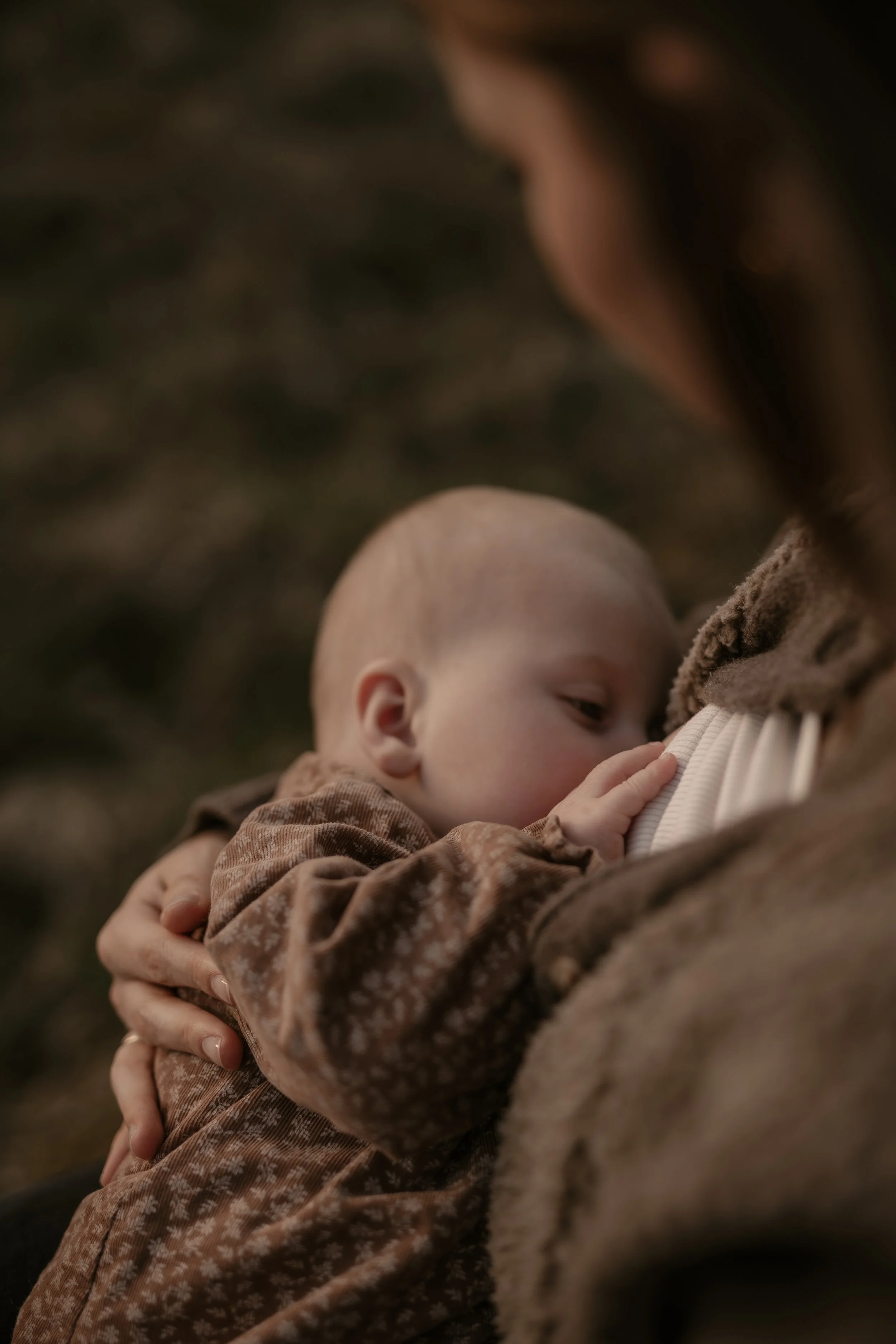 Ein Baby, das an die Brust eines Erwachsenen nuckelt, während es getragen wird, in einer natürlichen Umgebung.
