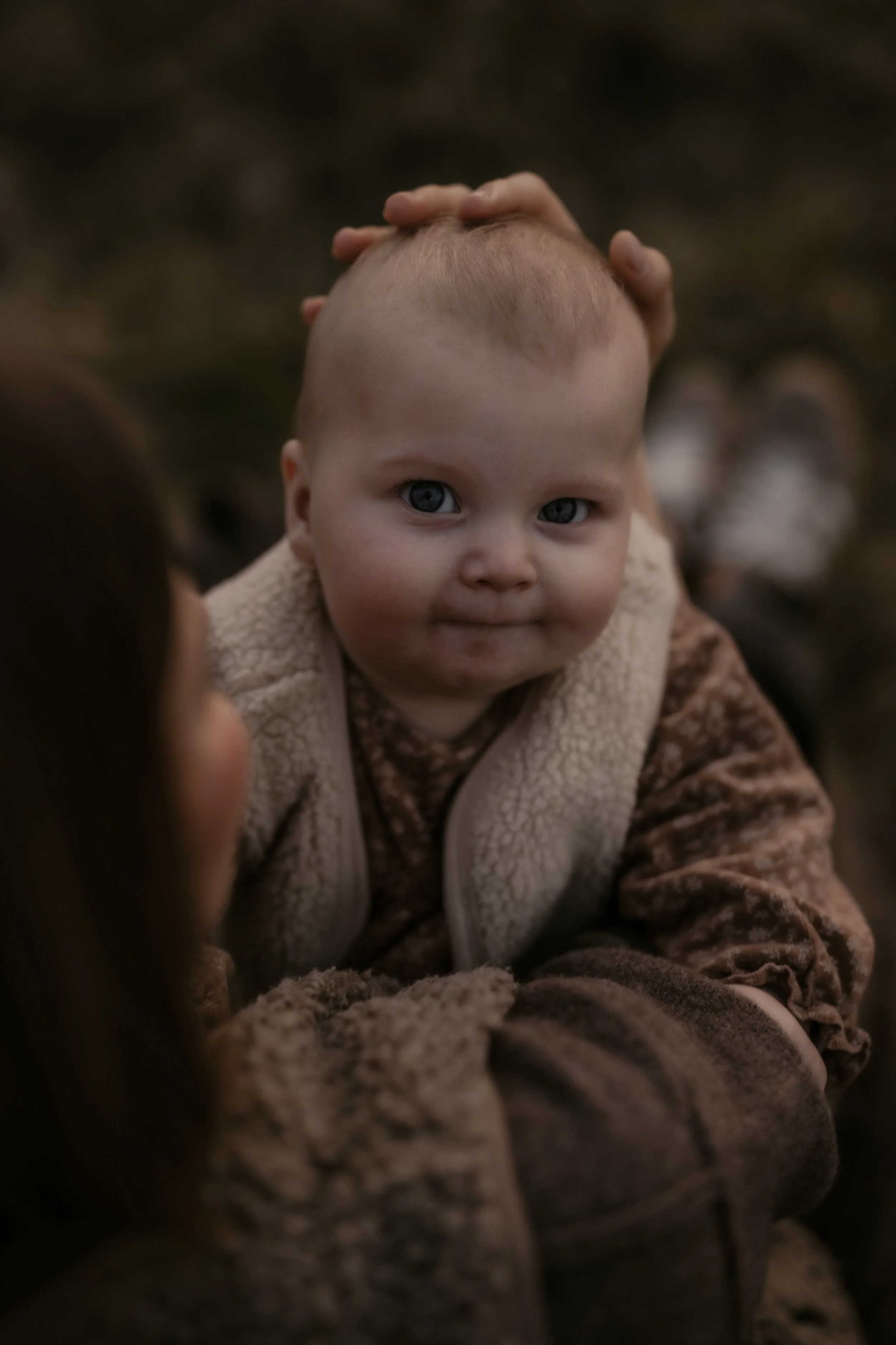 Ein kleines Baby mit blauen Augen, das von einer Person gehalten wird, draußen mit dunklem Hintergrund.