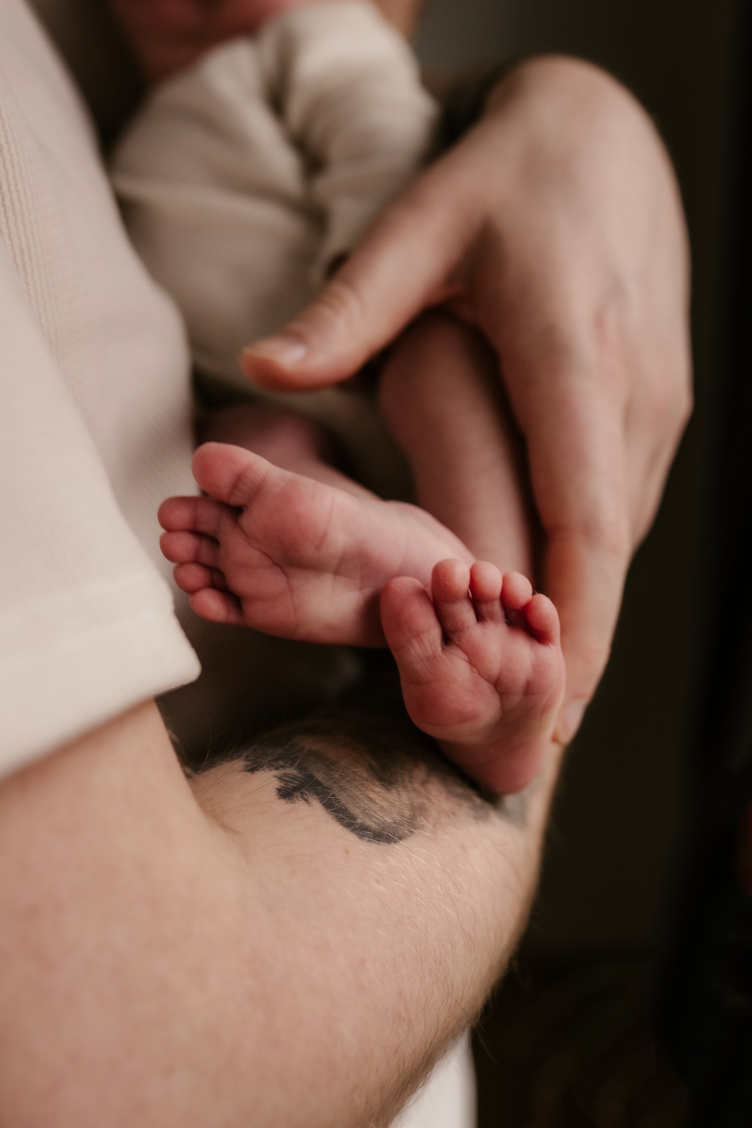 Nahaufnahme eines Babys, das auf einer erwachsenen Person liegt, die an einer Tätowierung auf dem Bauch kratzt oder leckt.