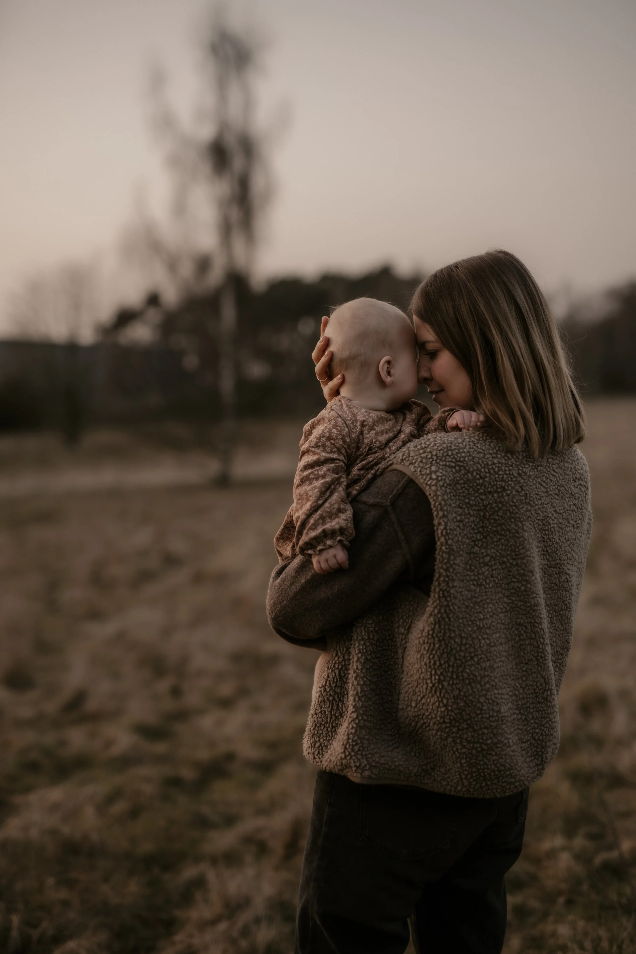 Frau hält Baby im Arm und berühren ihre Stirnen im Freien bei Sonnenuntergang.