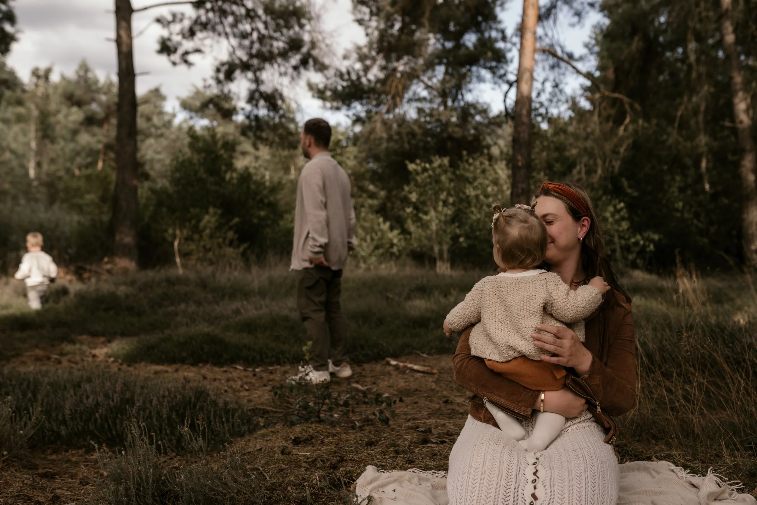 Familie im Wald, Frau hält kleines Mädchen im Arm, Mann im Hintergrund, Spaziergang in der Natur
