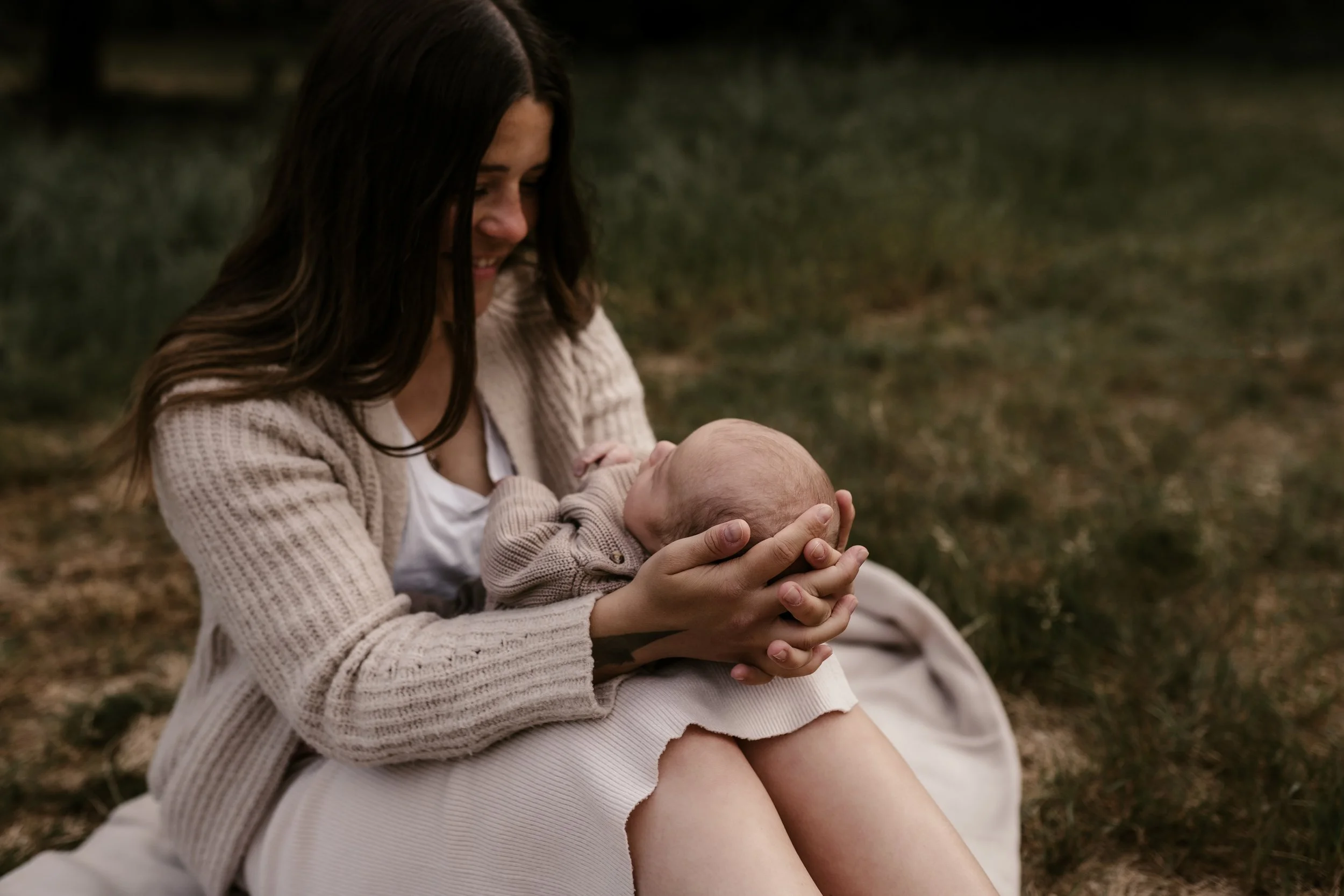 Eine junge Frau hält ein Baby auf ihren Beinen im Freien, beide lachen und genießen den Moment.