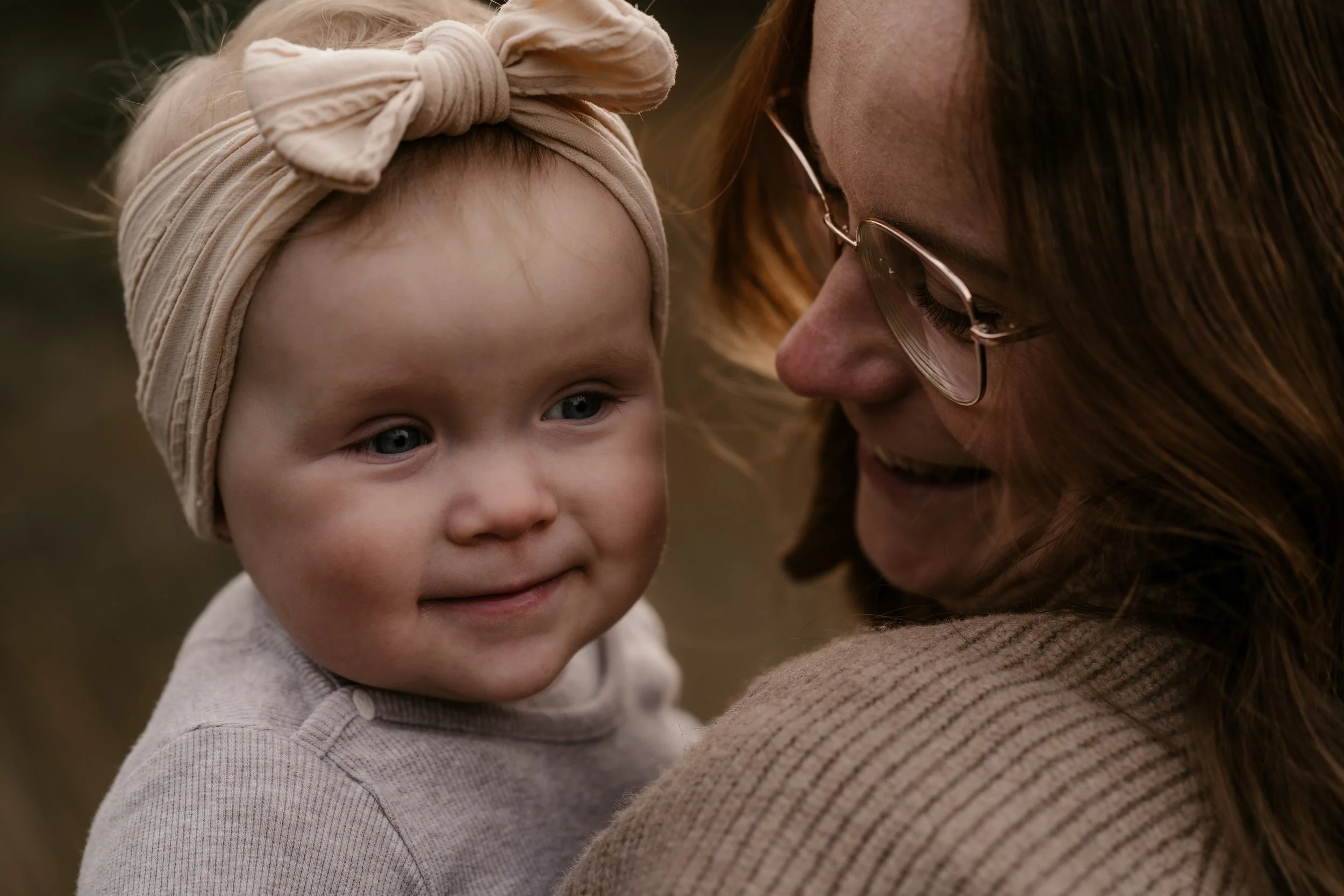 Eine junge Frau hält ein kleines Mädchen, das einen Beanie trägt, im Freien. Sie schauen sich liebevoll an.