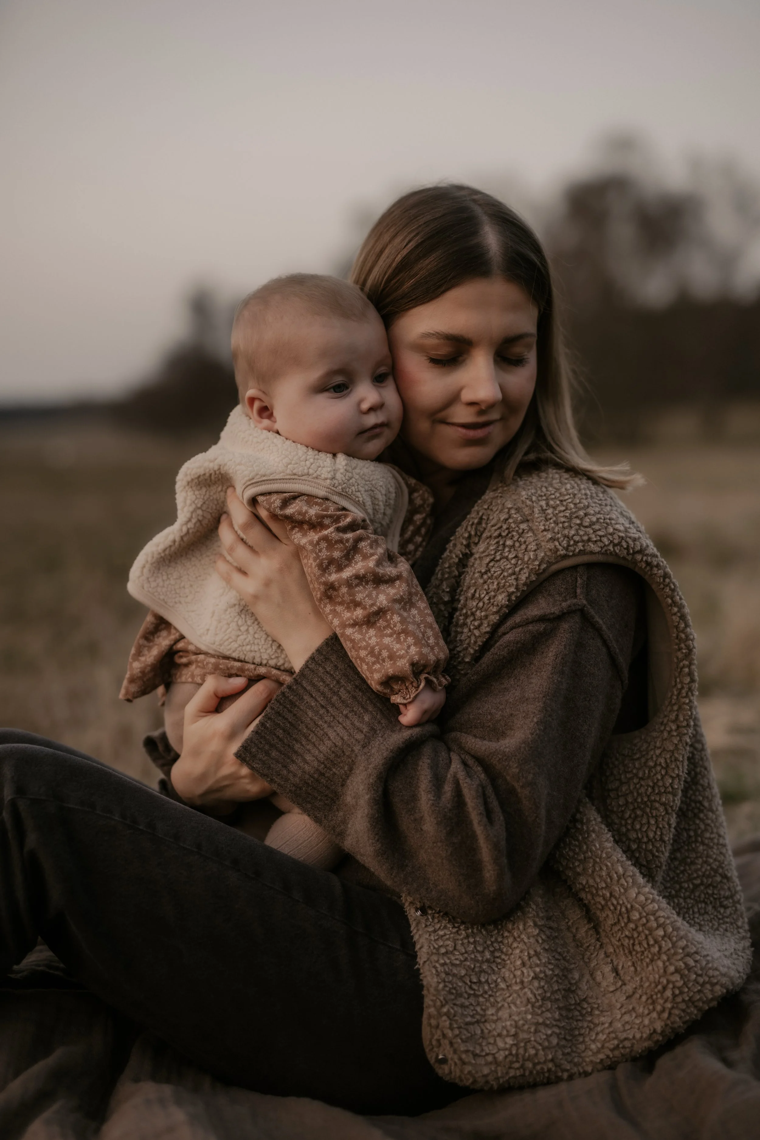 Eine Frau hält ein Baby im Arm im Freien bei Sonnenuntergang.