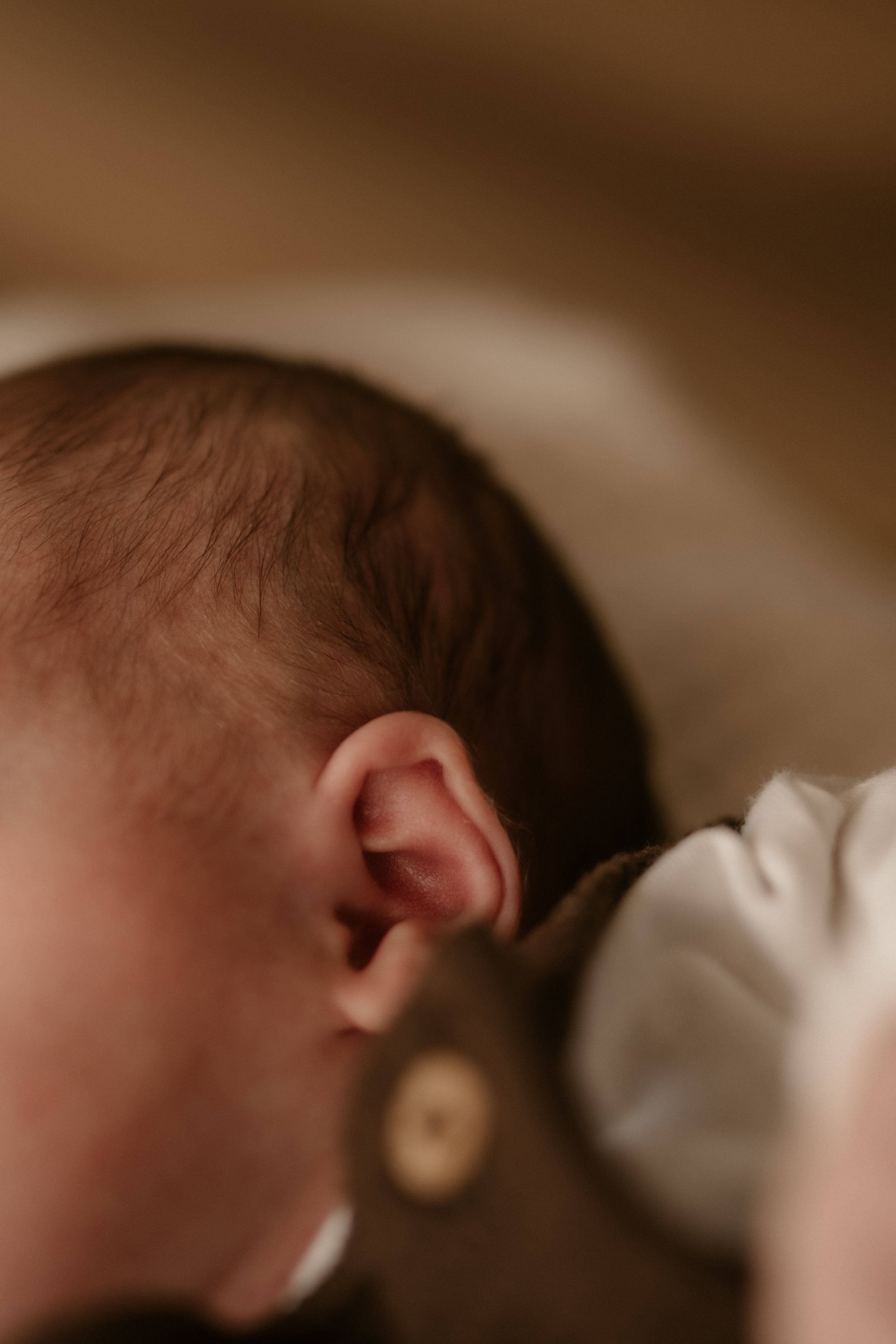 Nahaufnahme des Kopfes eines schlafenden Babys mit braunem Haar und Ohr, liegend auf einer weichen Decke.