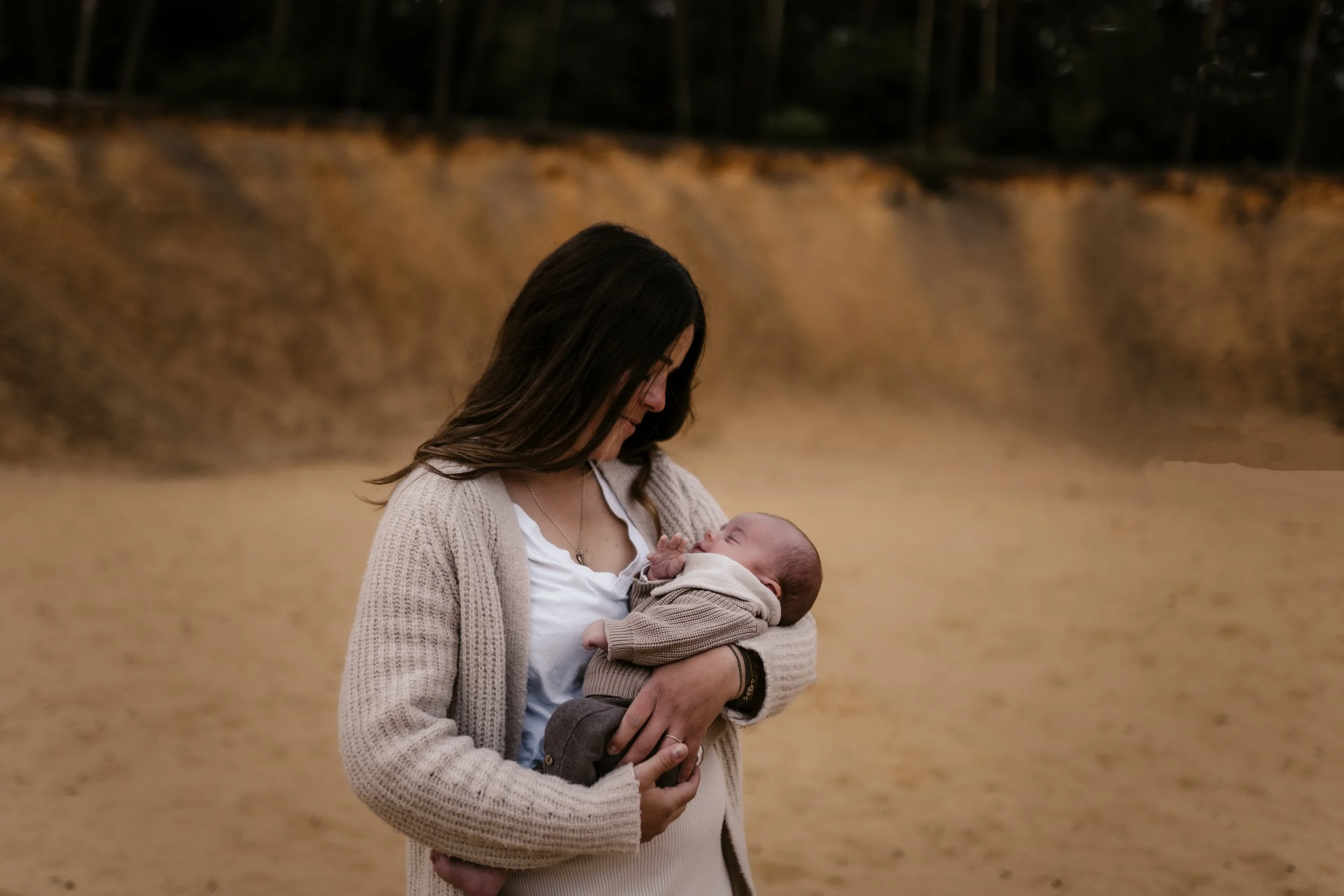 Eine Frau hält ein schlafendes Baby in den Armen, im Hintergrund eine Wasserfall-ähnliche Felsenwand.