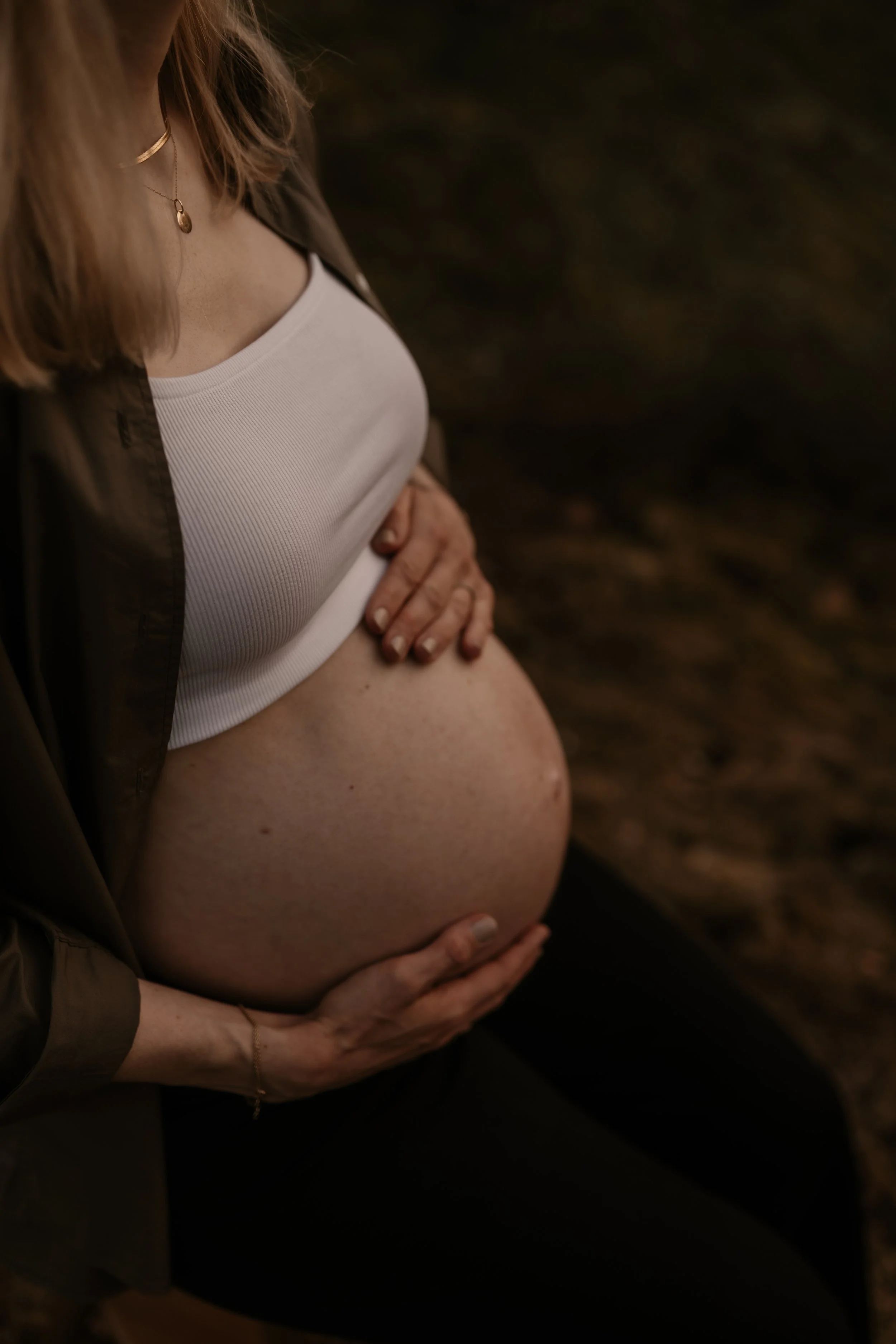 Eine schwangere Frau, die ihren Bauch hält, während sie sich an einem dunklen Ort befindet.