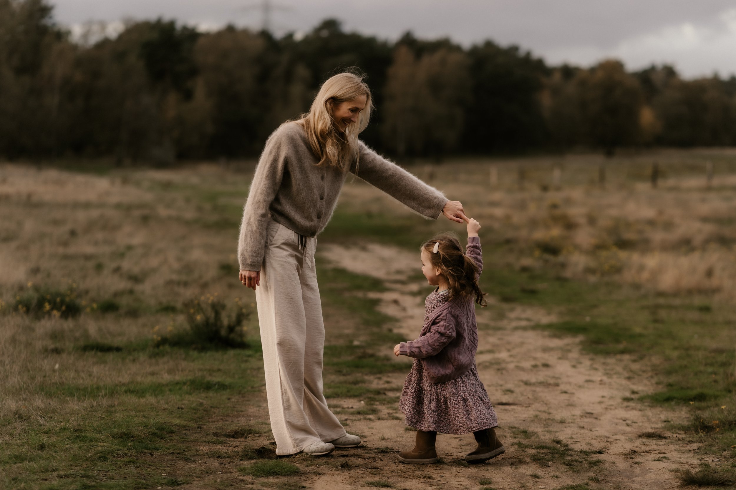 Eine ältere Frau tanzt mit einem kleinen Mädchen auf einem Feld bei Sonnenuntergang, während sie sich gegenseitig im Arm halten.