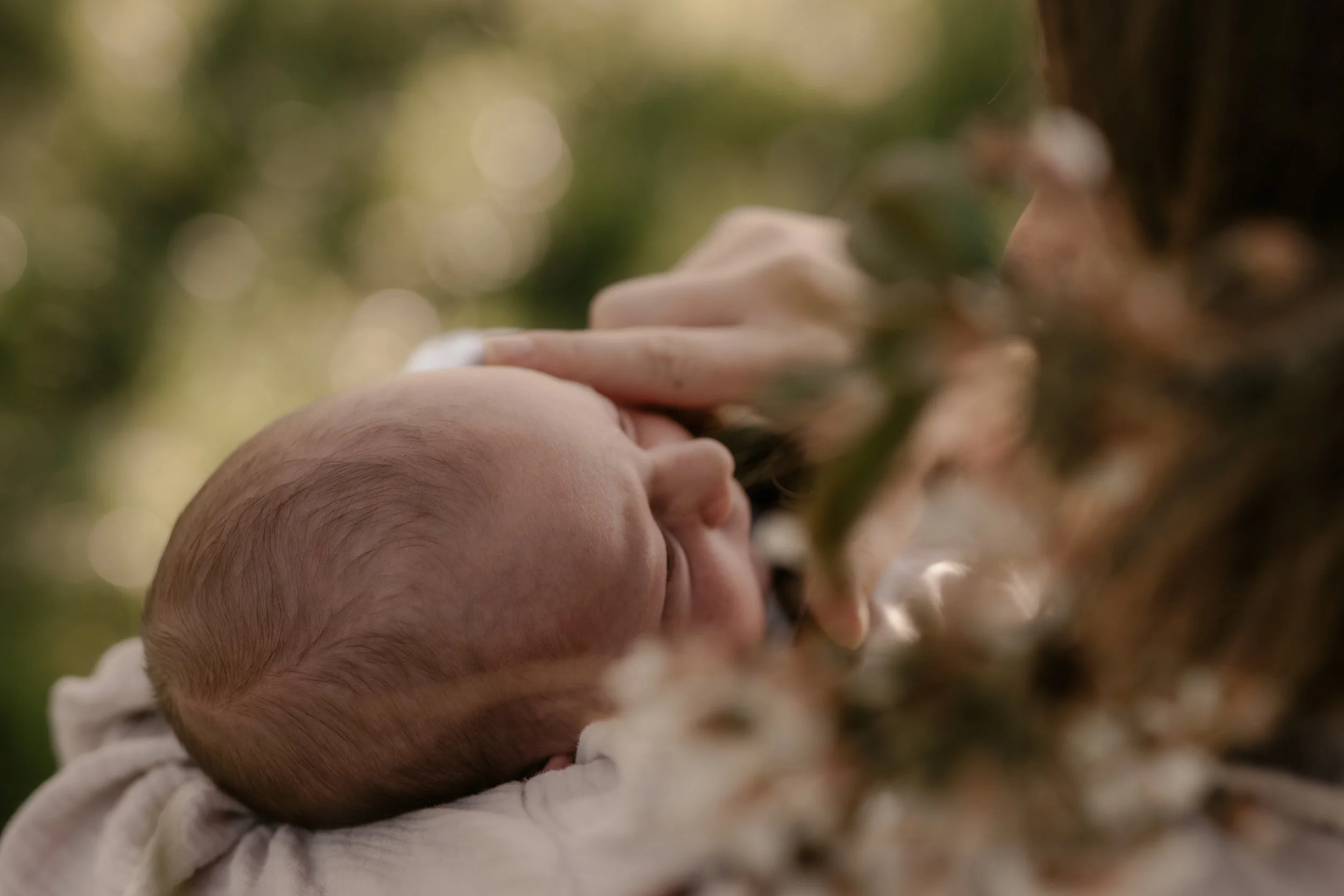 Ein Baby wird von einer Person an einem sonnigen Tag im Freien gehalten.