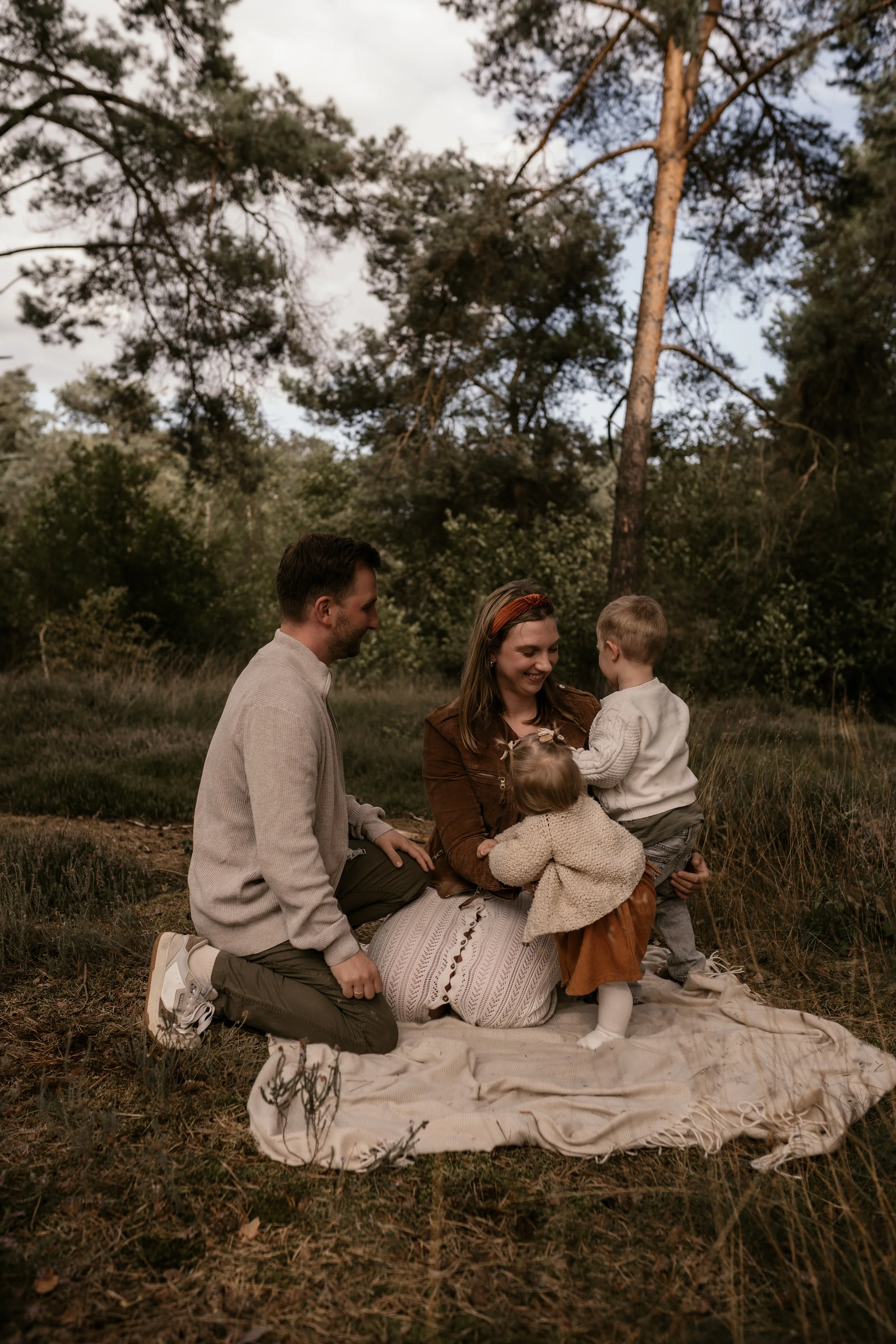 Familie mit zwei kleinen Kindern sitzt auf einer Decke im Wald und hat Spaß.