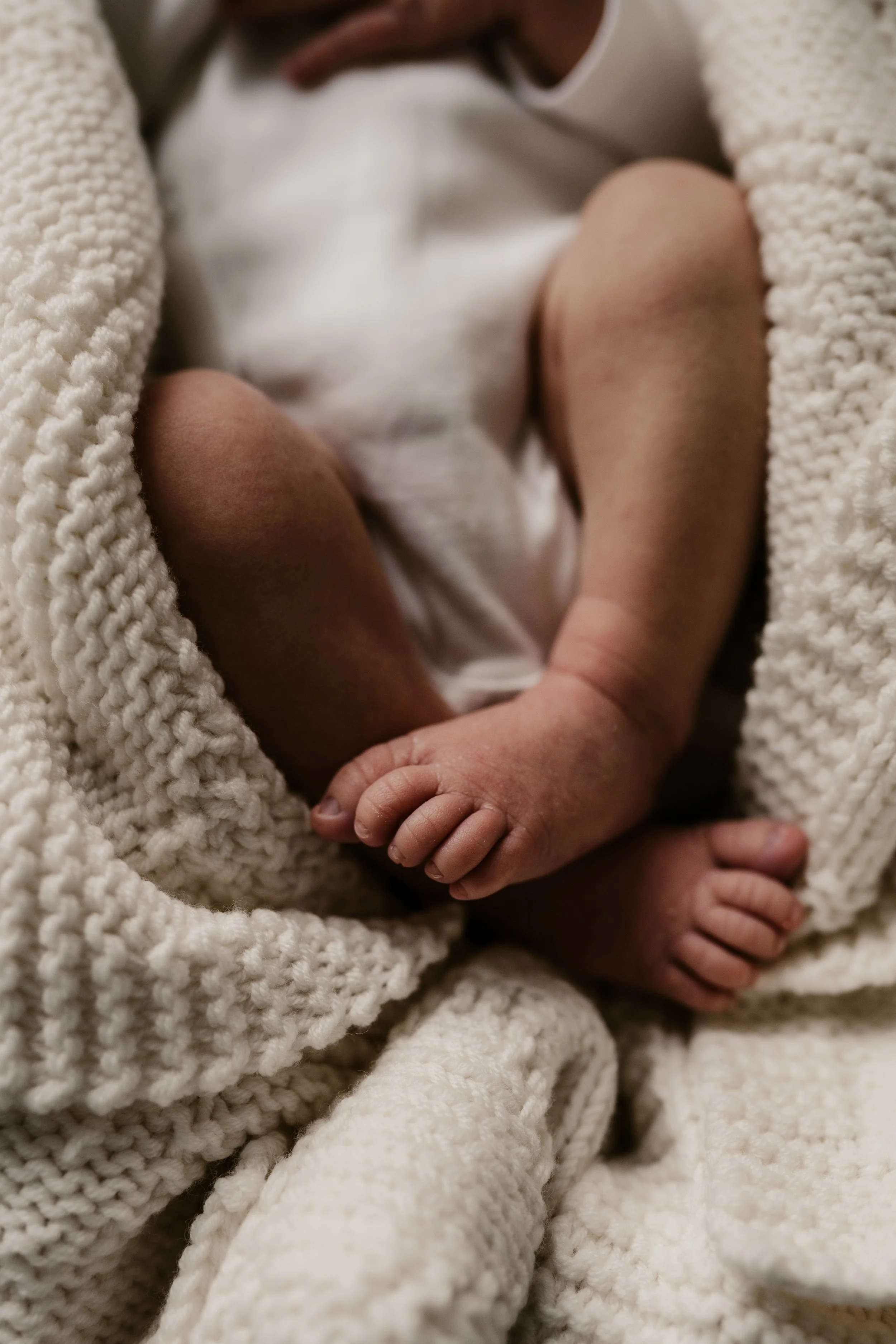 Nahaufnahme eines Neugeborenen, eingewickelt in eine cremefarbene, gestrickte Decke.