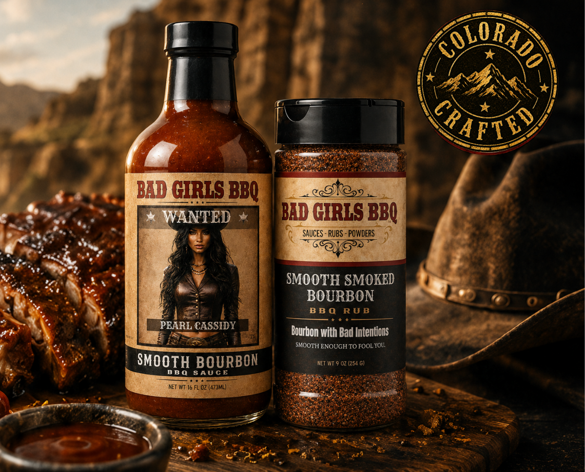 Two bottles of barbecue sauce from the brand Bad Girls BBQ, one labeled Pearl Cassidy and the other labeled with bourbon flavor. The bottles are set against a rustic background with a piece of cooked barbecue meat nearby and a cowboy hat in the background. There is a Colorado Crafted seal in the top right corner.