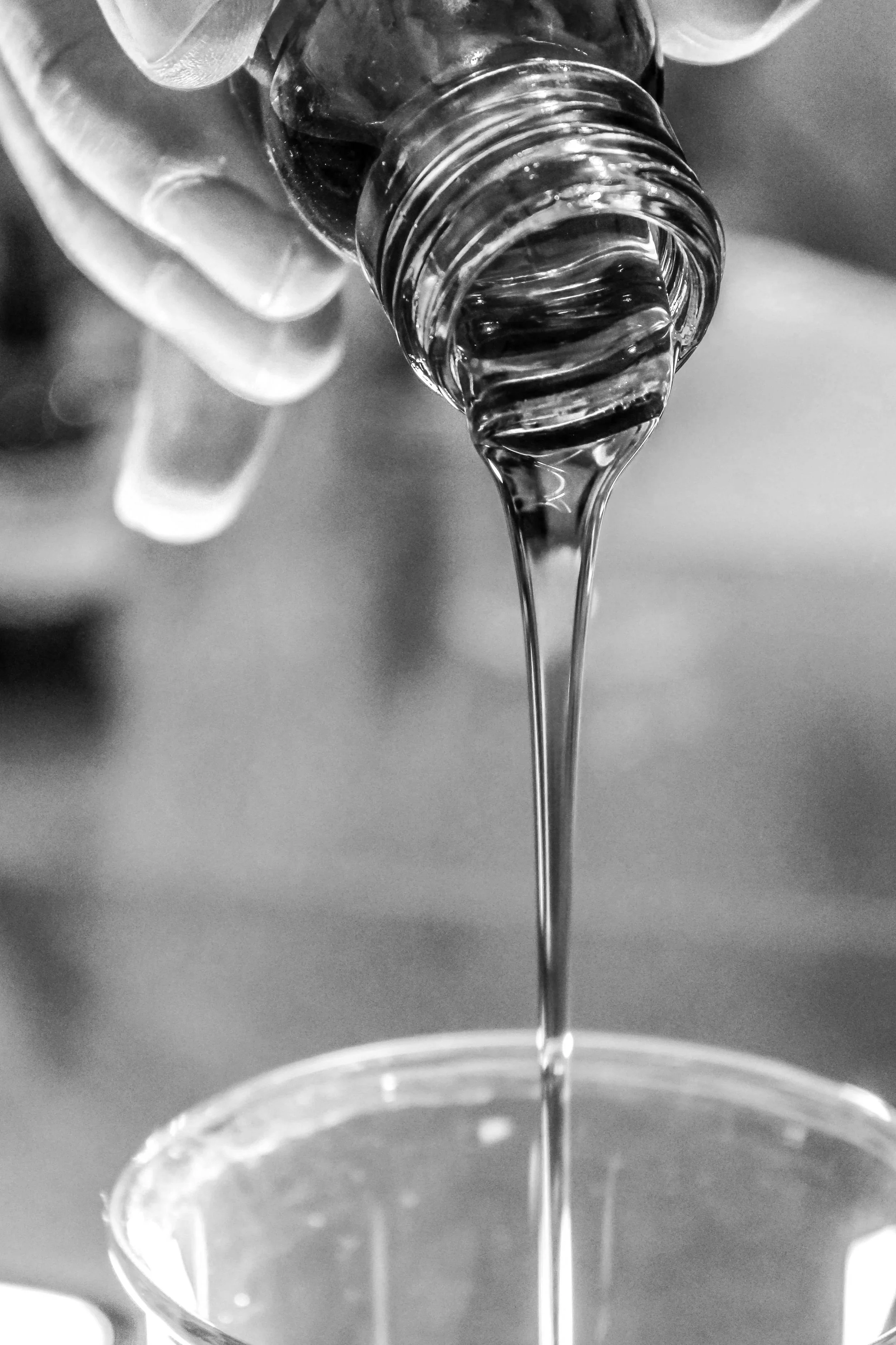 Black and white photo of clear liquid pouring from a plastic bottle into a glass.