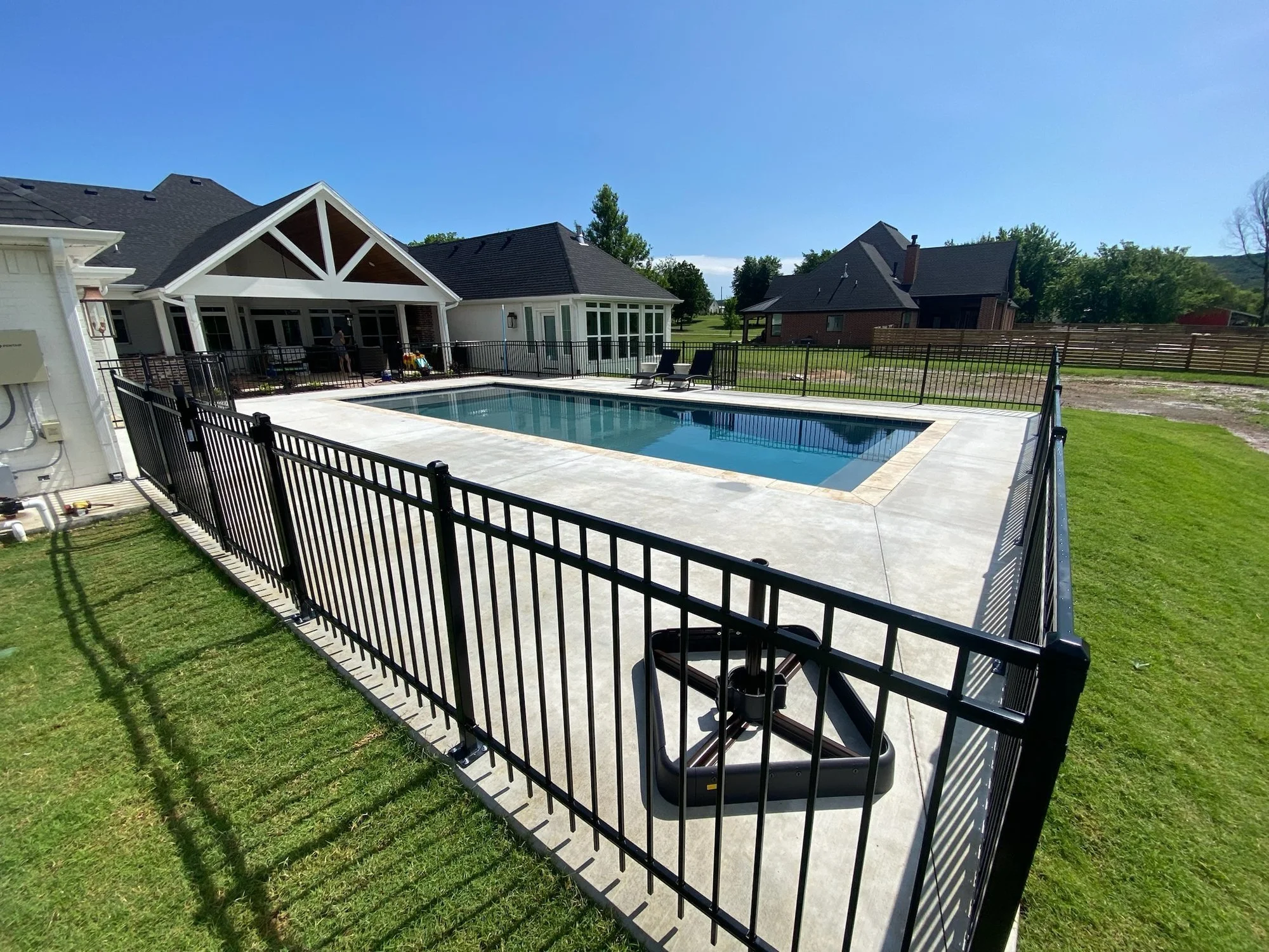Black steel picket fence enclosing a concrete pool deck behind a home.