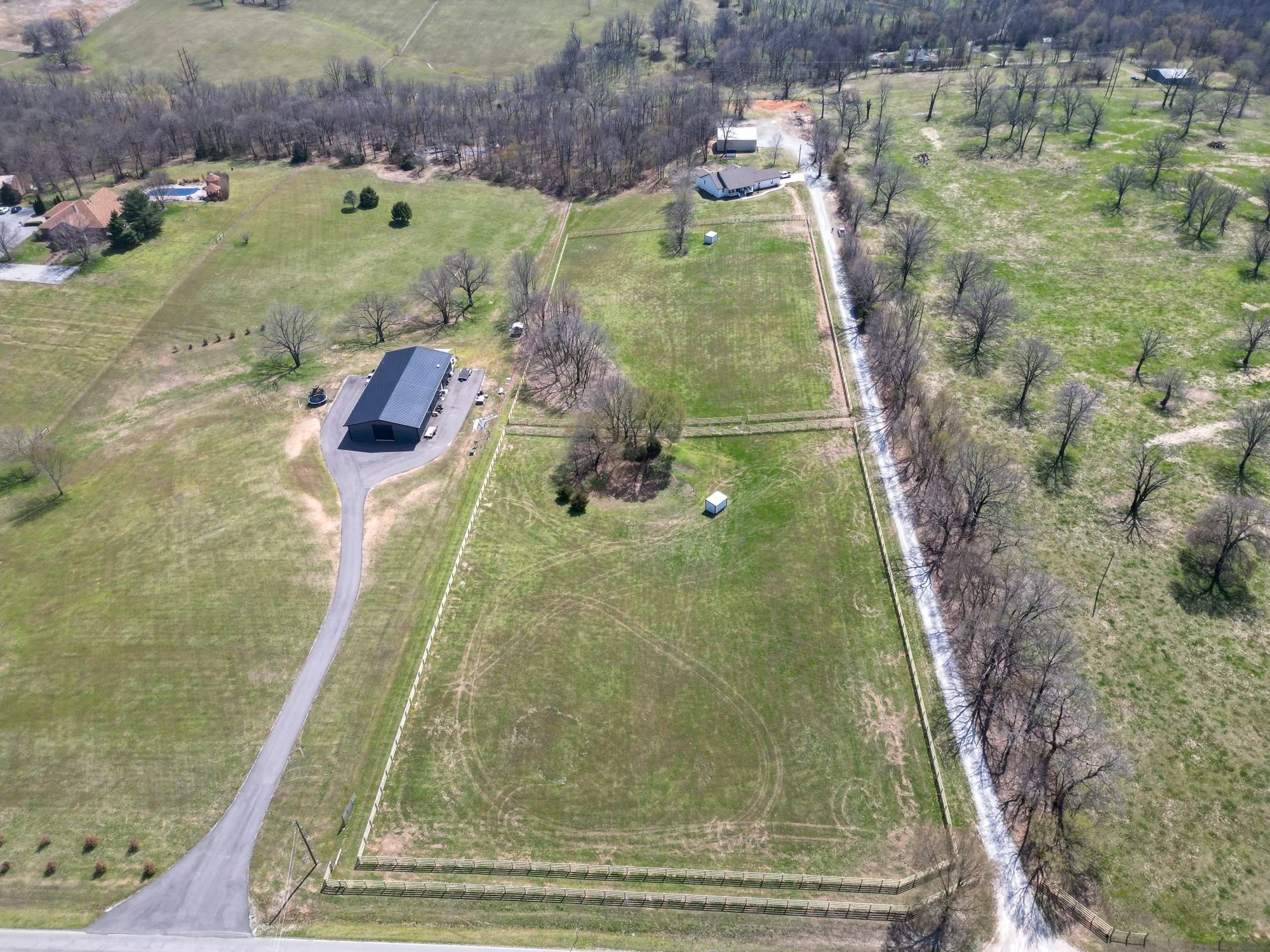 Aerial view of fenced acreage with a metal building, gravel drive, and fenced pasture lines.