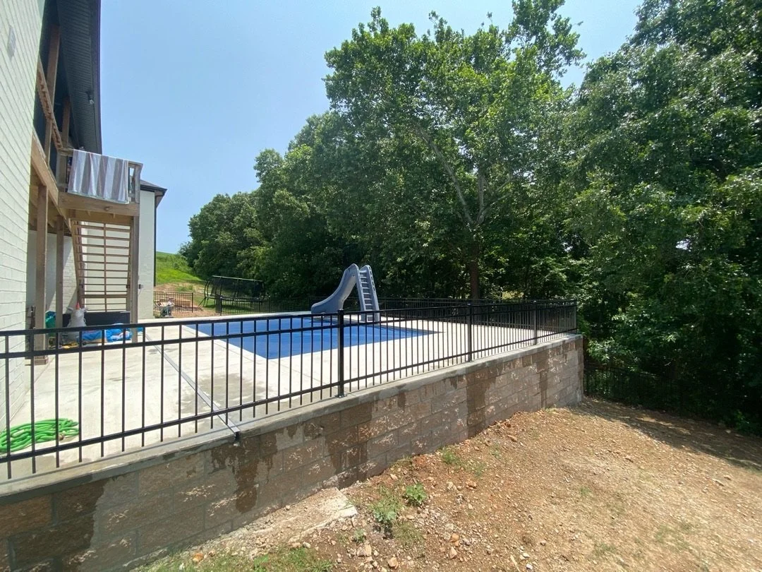 Black steel fence along the top of a block wall around a pool deck.