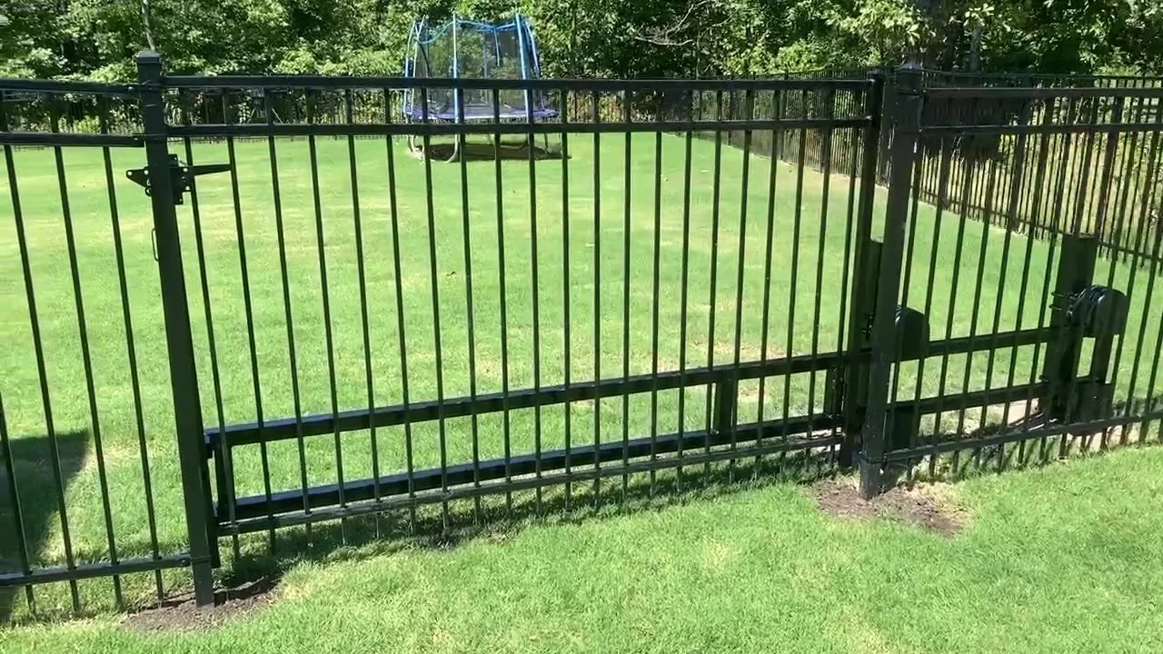 Black steel gate set in a black picket fence along a grassy yard.