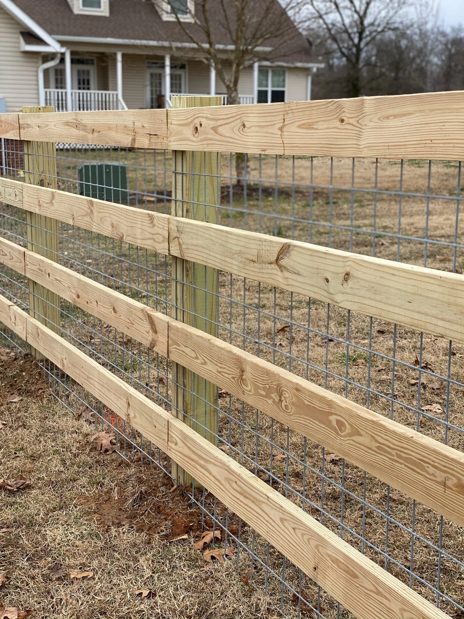 Three-board wood fence backed with welded wire panels, on treated wood posts.