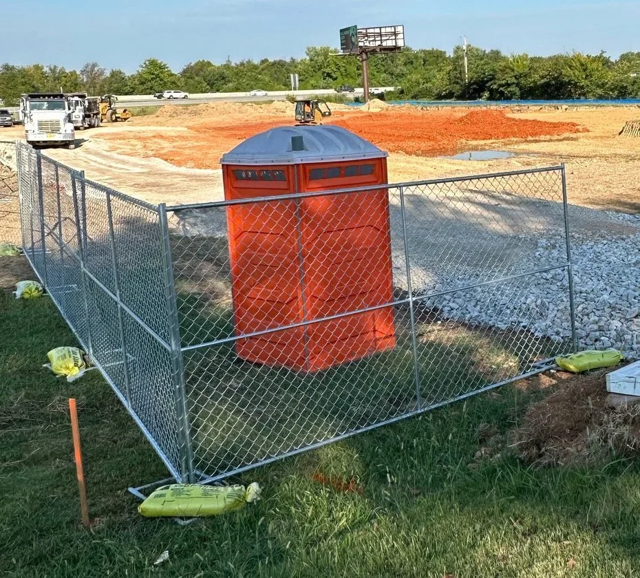 Temporary chain link fence panels around a portable restroom on a commercial construction site
