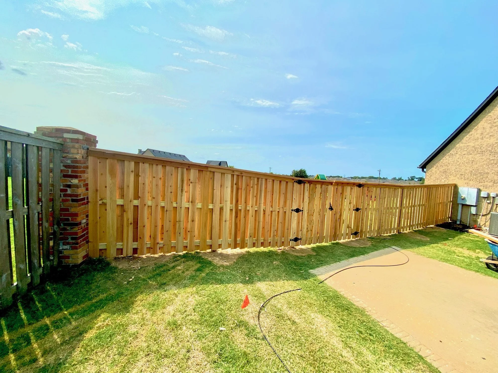 New wood privacy fence with a walk gate enclosing a backyard next to a brick column and concrete patio.