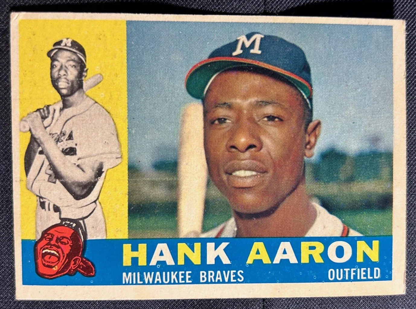Vintage baseball card featuring Hank Aaron of the Milwaukee Braves, showing his portrait on the right and a black-and-white action image of him holding a bat on the left, with a team logo at the bottom.