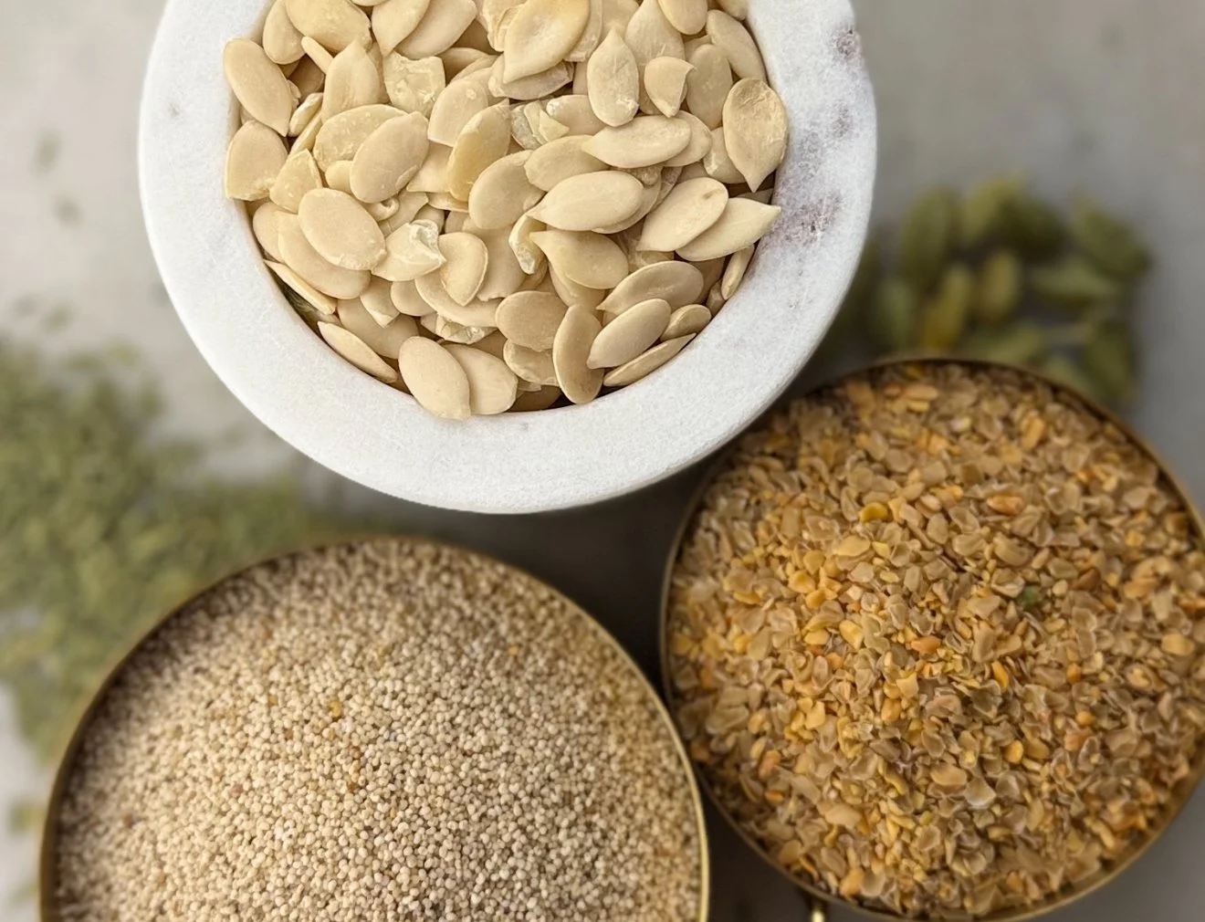 Close-up of various seeds and grains in bowls, including poppy seeds, fenugreek seeds, and melon seeds.