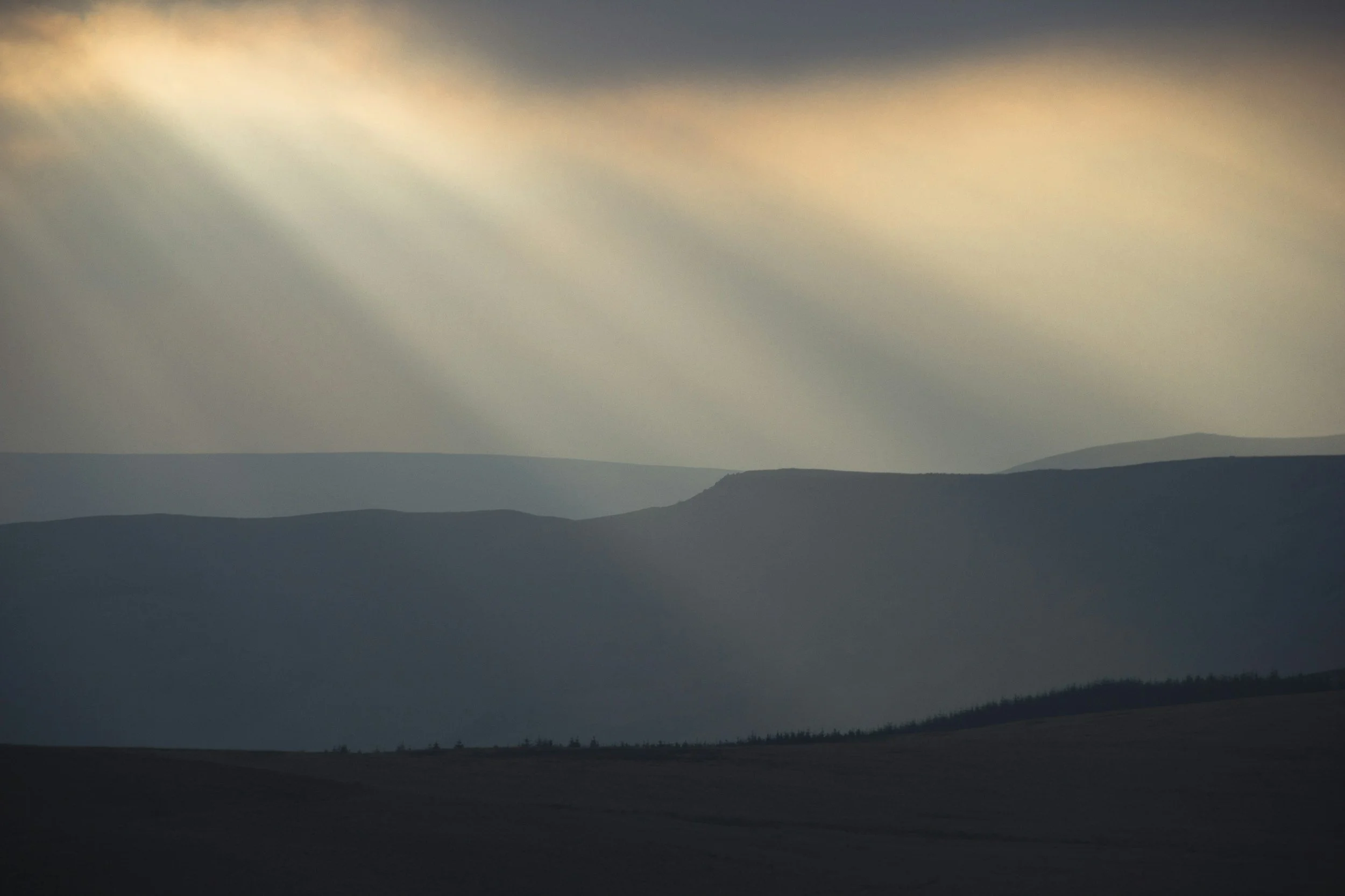 Landscape of layered mountains under a cloudy sky with sunlight rays breaking through.