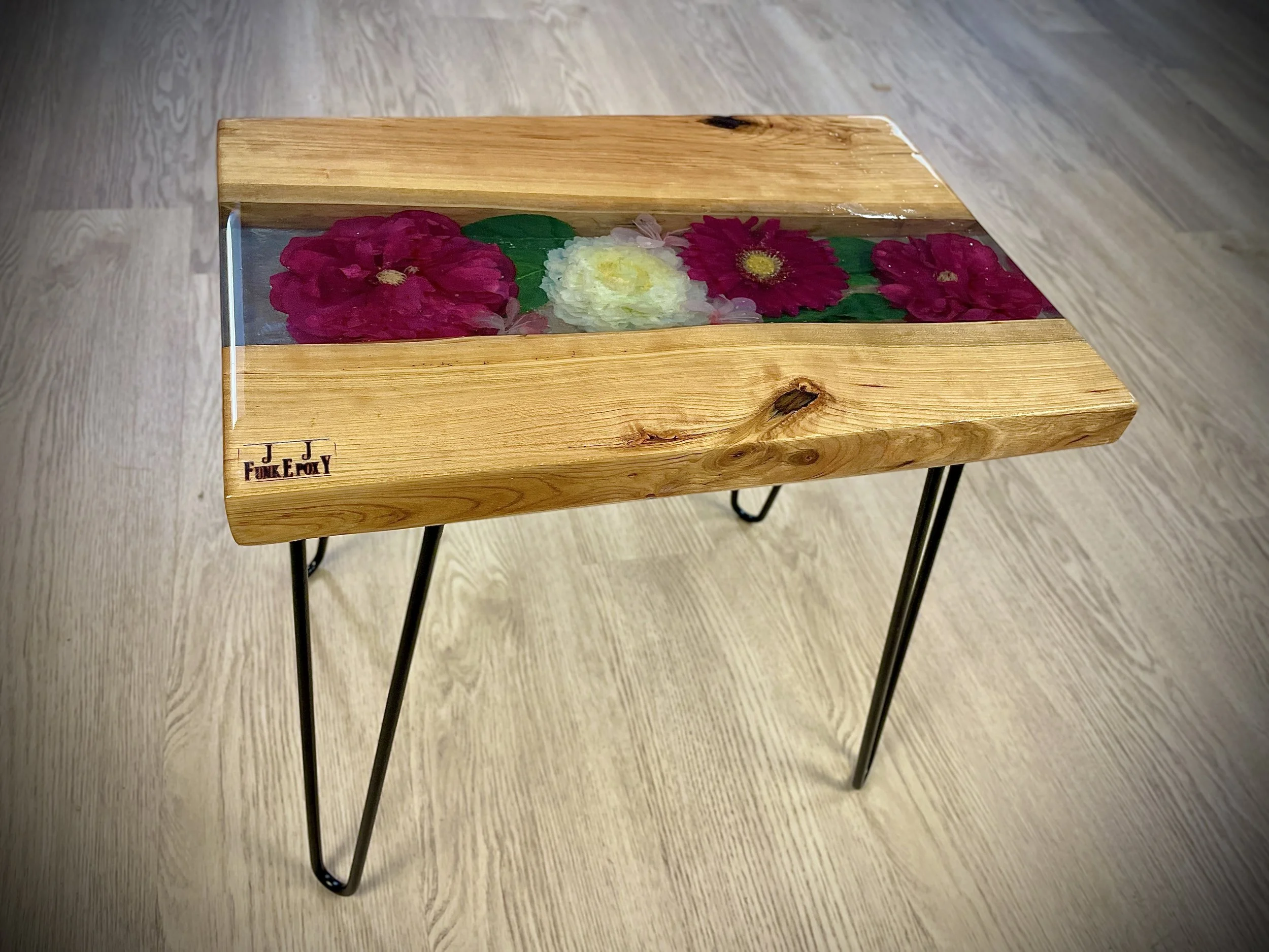 Wooden table with metal hairpin legs and a resin inlay top featuring colorful flowers.