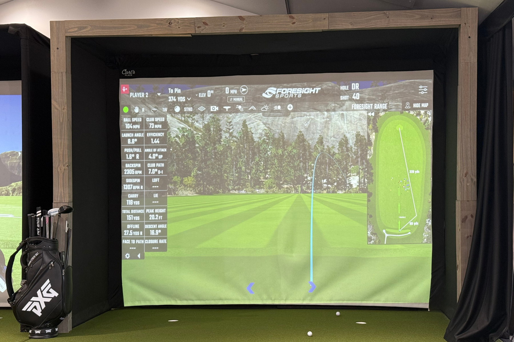Golf simulator screen displaying a shot trajectory, distance, and yardage on a virtual golf course with a set of golf clubs on the left.