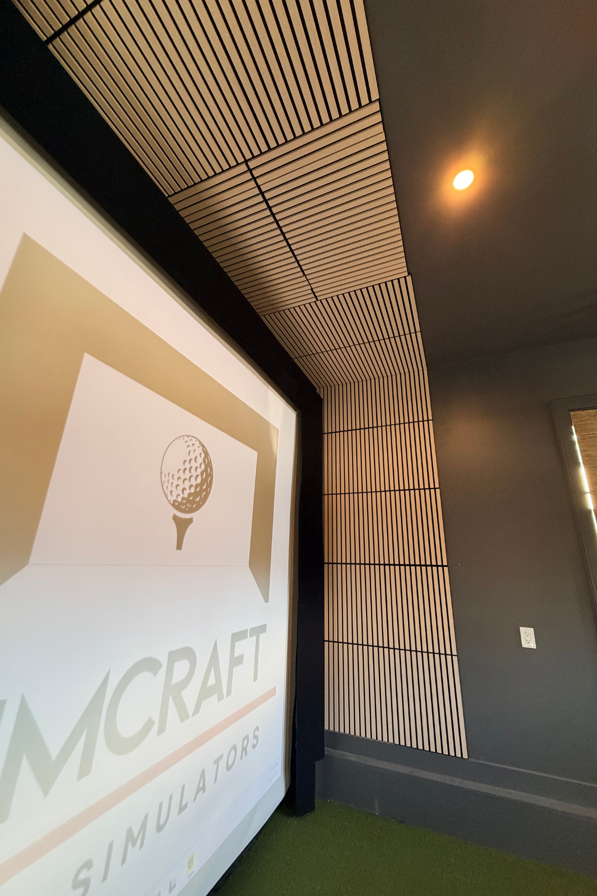 Projection screen displaying a log, featuring a golf ball on a tee, in a modern room with wooden paneling on the ceiling and wall, a small ceiling light, and green carpet.