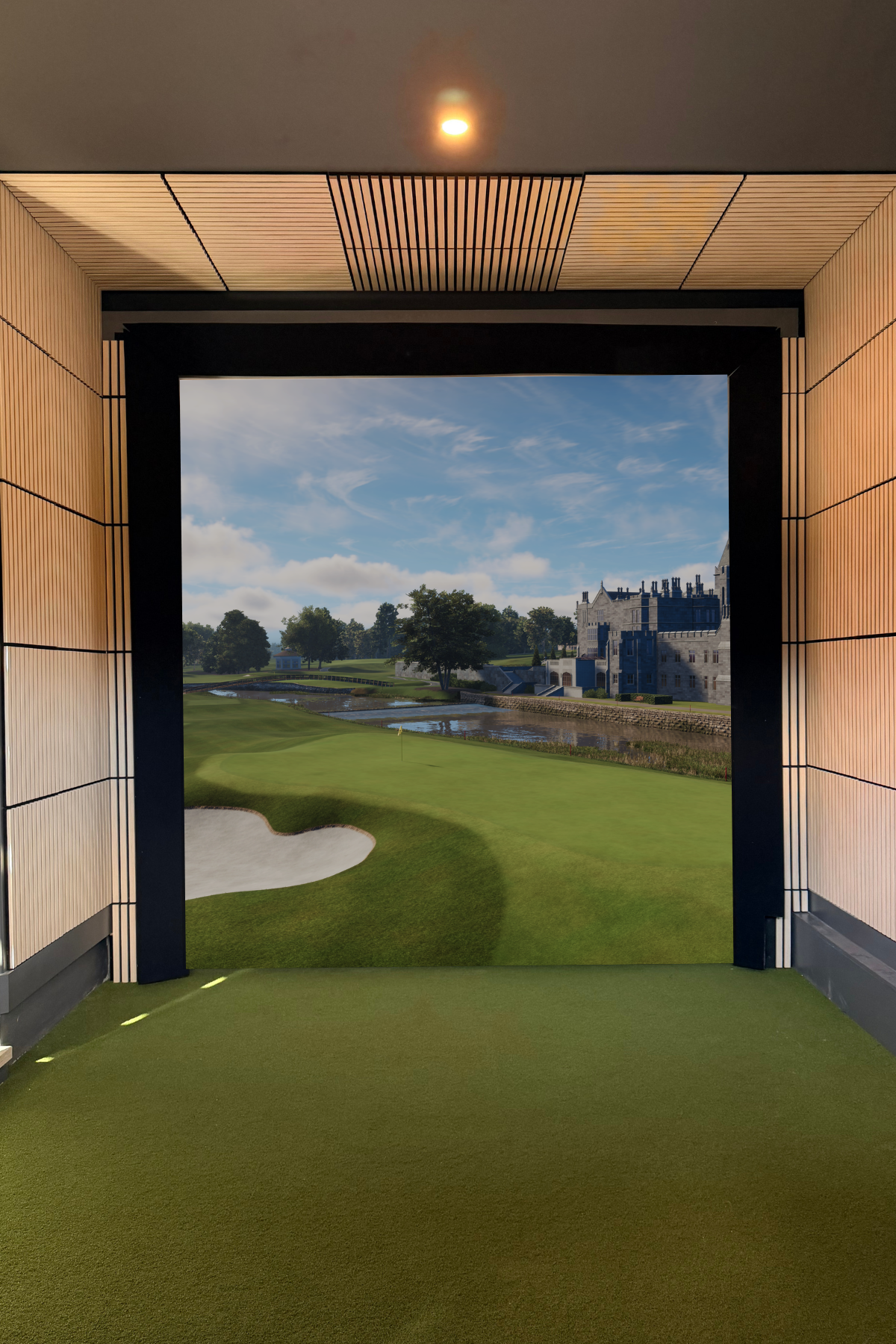 Indoor view of a golf simulator room showing a virtual golf course with green grass, trees, water, a sand trap, and a castle-like building in the distance, through a large window.