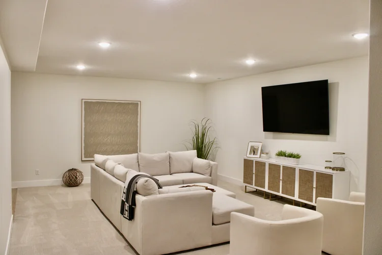 Basement living area with light walls and recessed ceiling lights