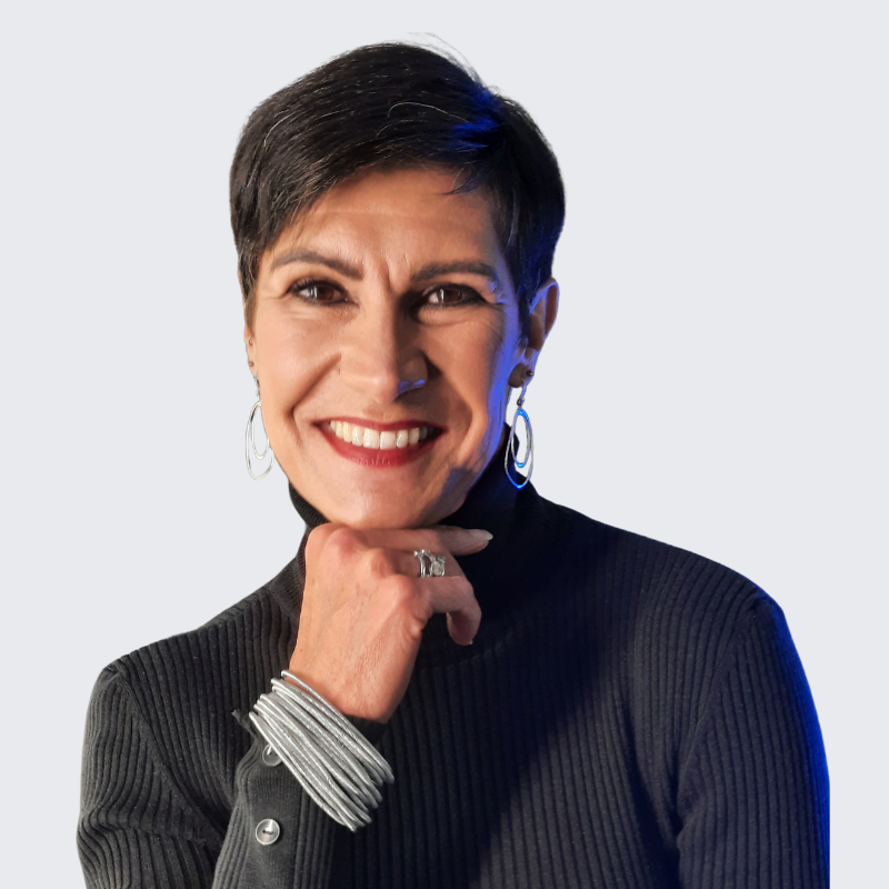 A woman with short dark hair, wearing a black turtleneck sweater, smiling with her hand under her chin.