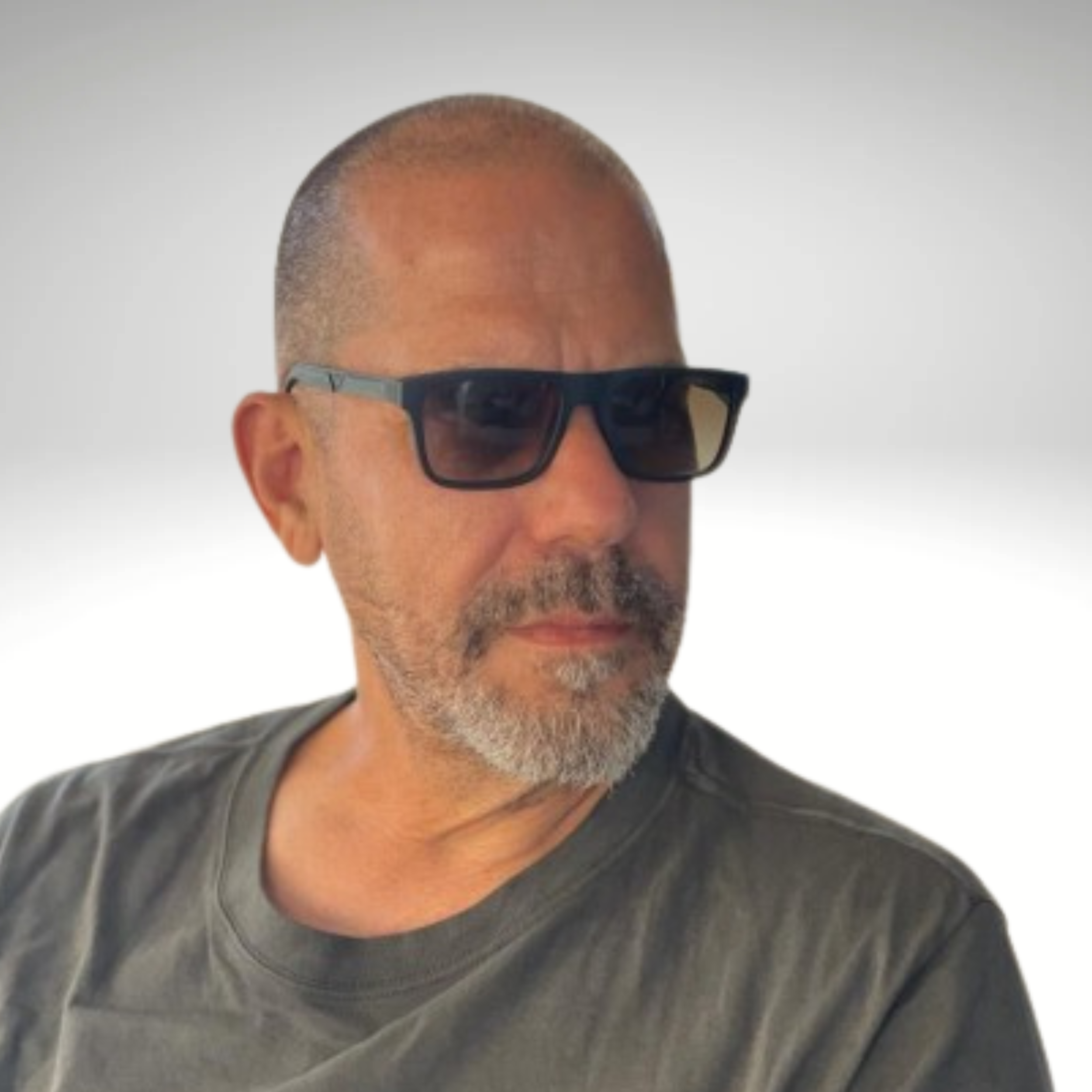 A man with a shaved head, gray beard, wearing black sunglasses and a dark T-shirt, looking to the side against a plain light background.