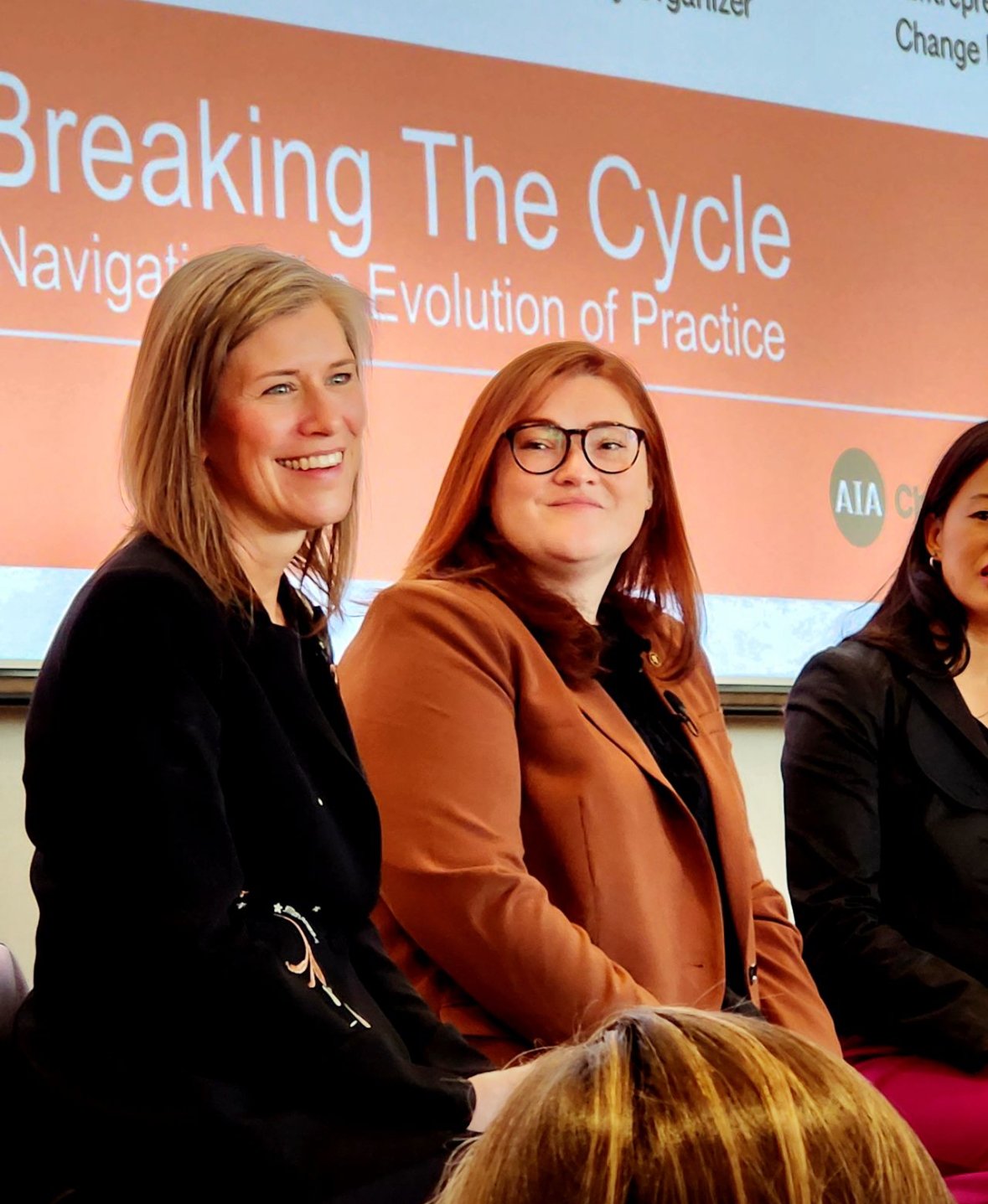 Three women sitting at a panel during a presentation, with a large screen behind them displaying the words 'Breaking The Cycle' and 'Navigation of the Evolution of Practice'.
