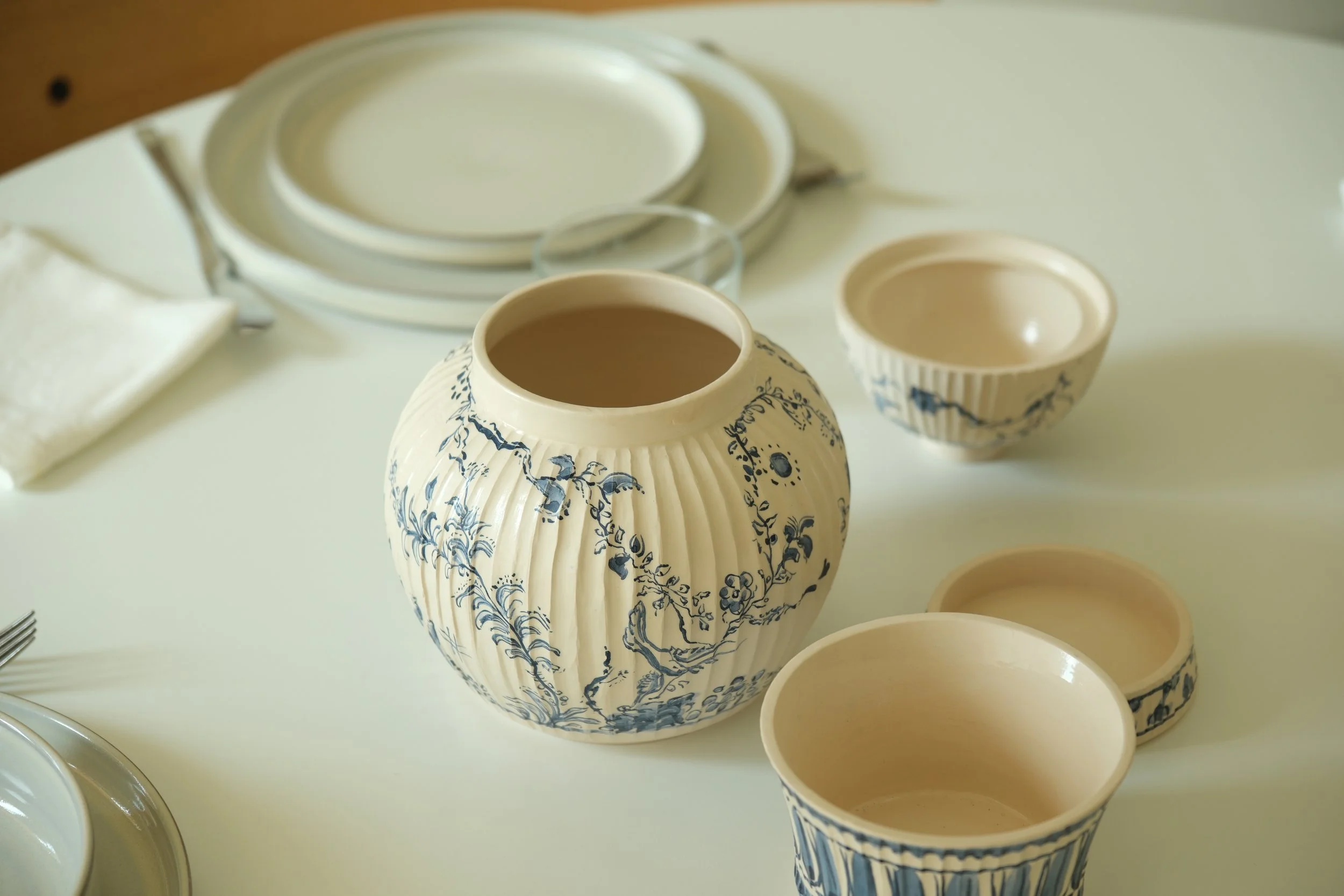 Vasos de cerâmica decorativos com padrões azuis e brancos, com alguns contendo líquidos, colocados sobre uma superfície clara