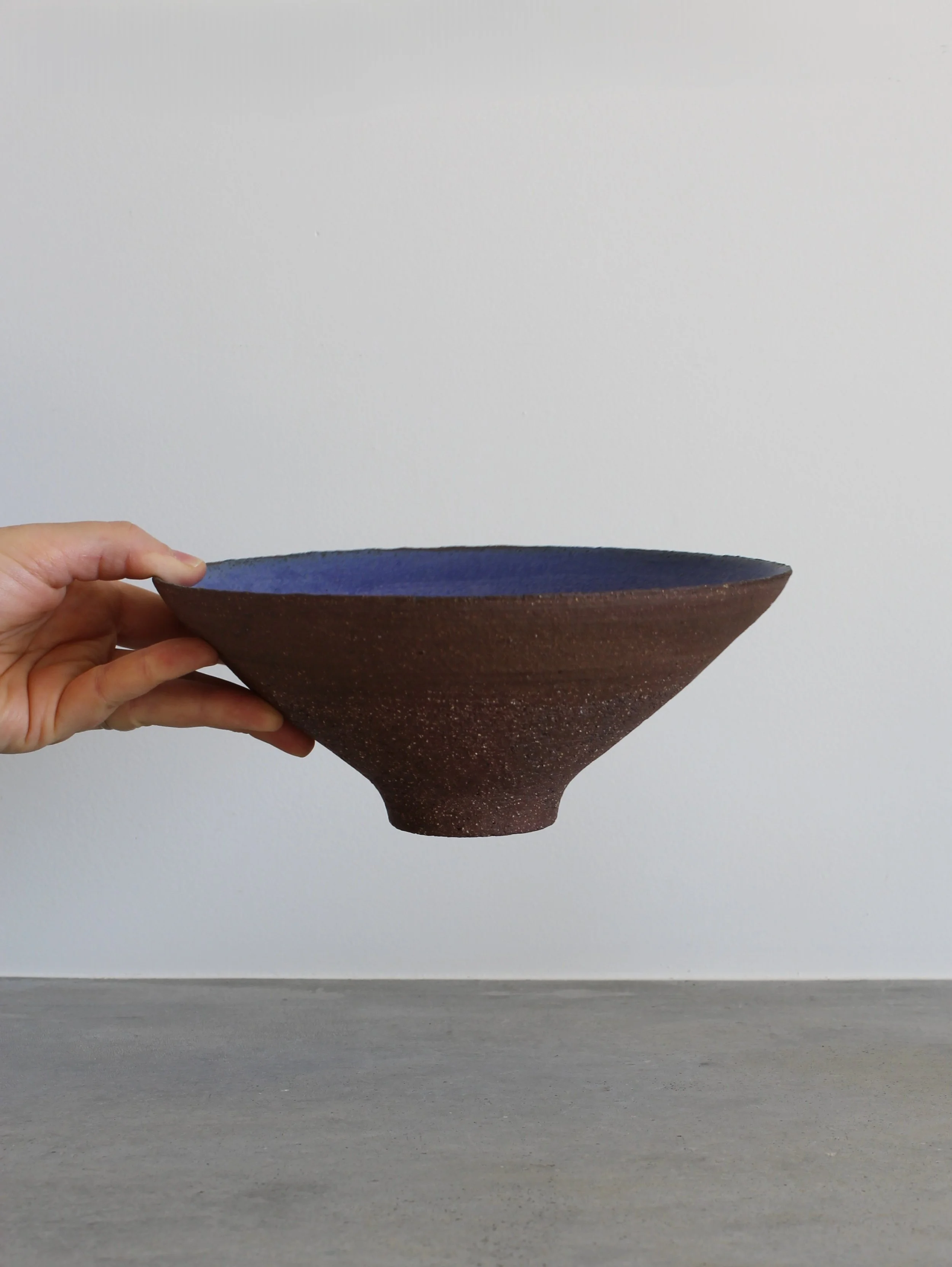 Mão a segurar o Centro Cónico Azul Cobalto de perfil para mostrar a silhueta geométrica e escala - Handmade Ceramics Portugal - Feitiu