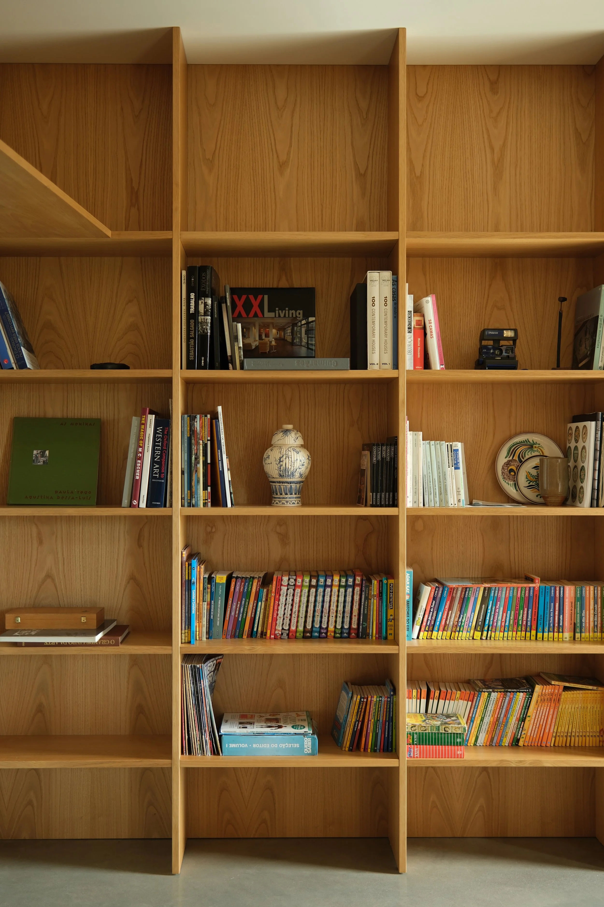 Estante de madeira com livros e objetos decorativos, incluindo uma jarra de cerâmica, uma placa decorativa e uma máquina de escrever.