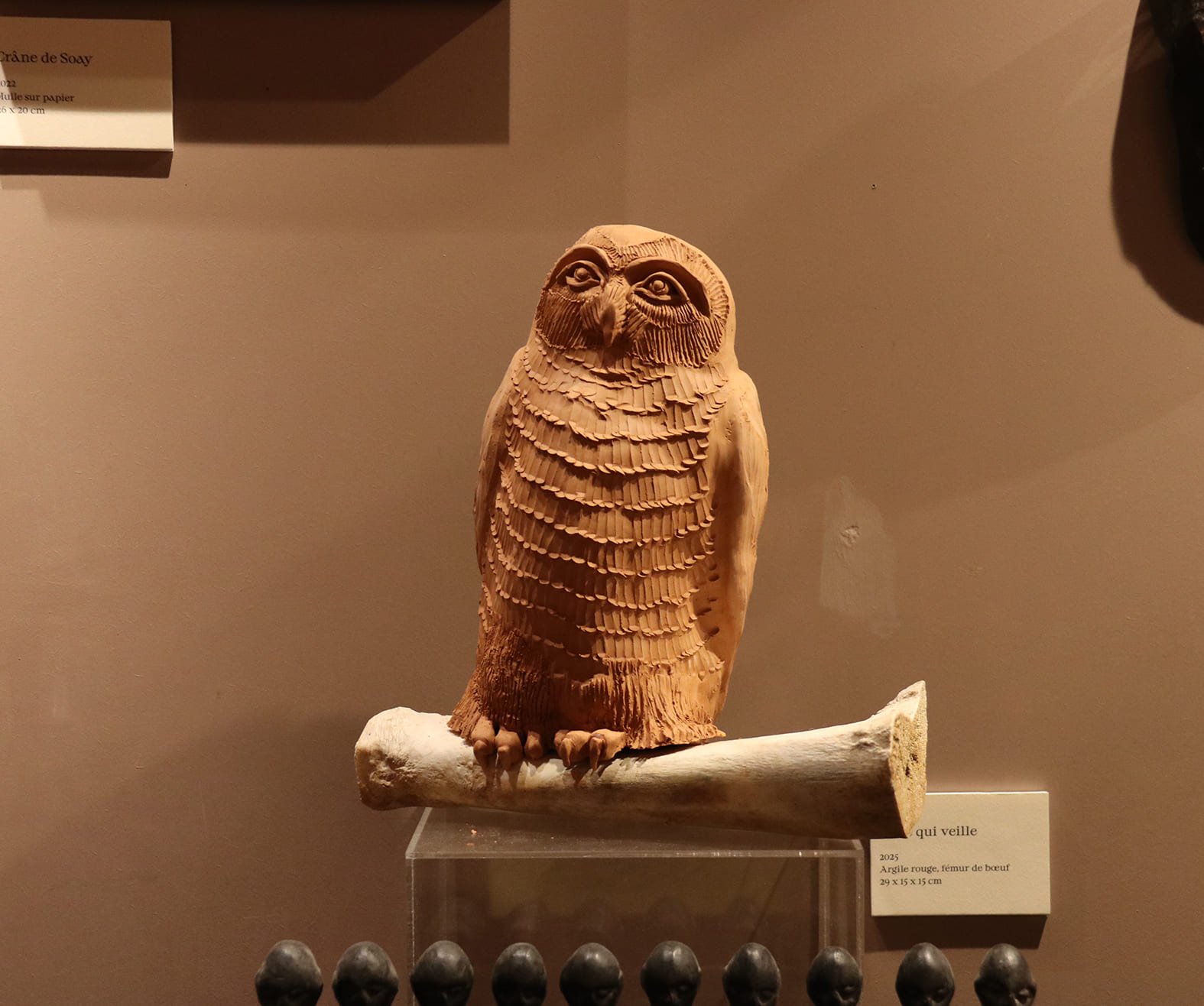 Sculpture en argile d'une chouette perchée sur une branche, exposée dans un musée.