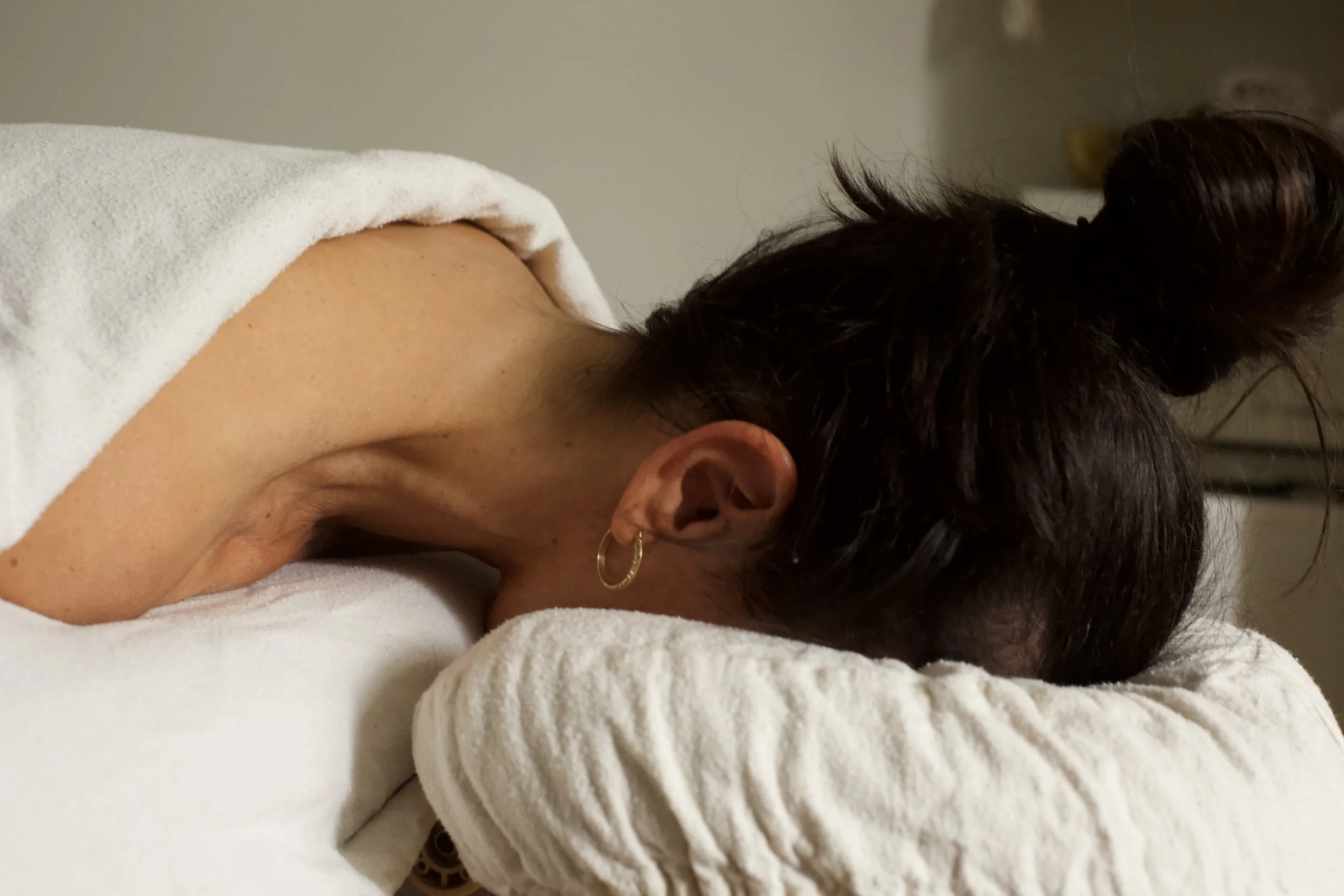 Femme recevant un massage sur un lit, avec une serviette blanche sur le dos et des cheveux noirs en chignon.