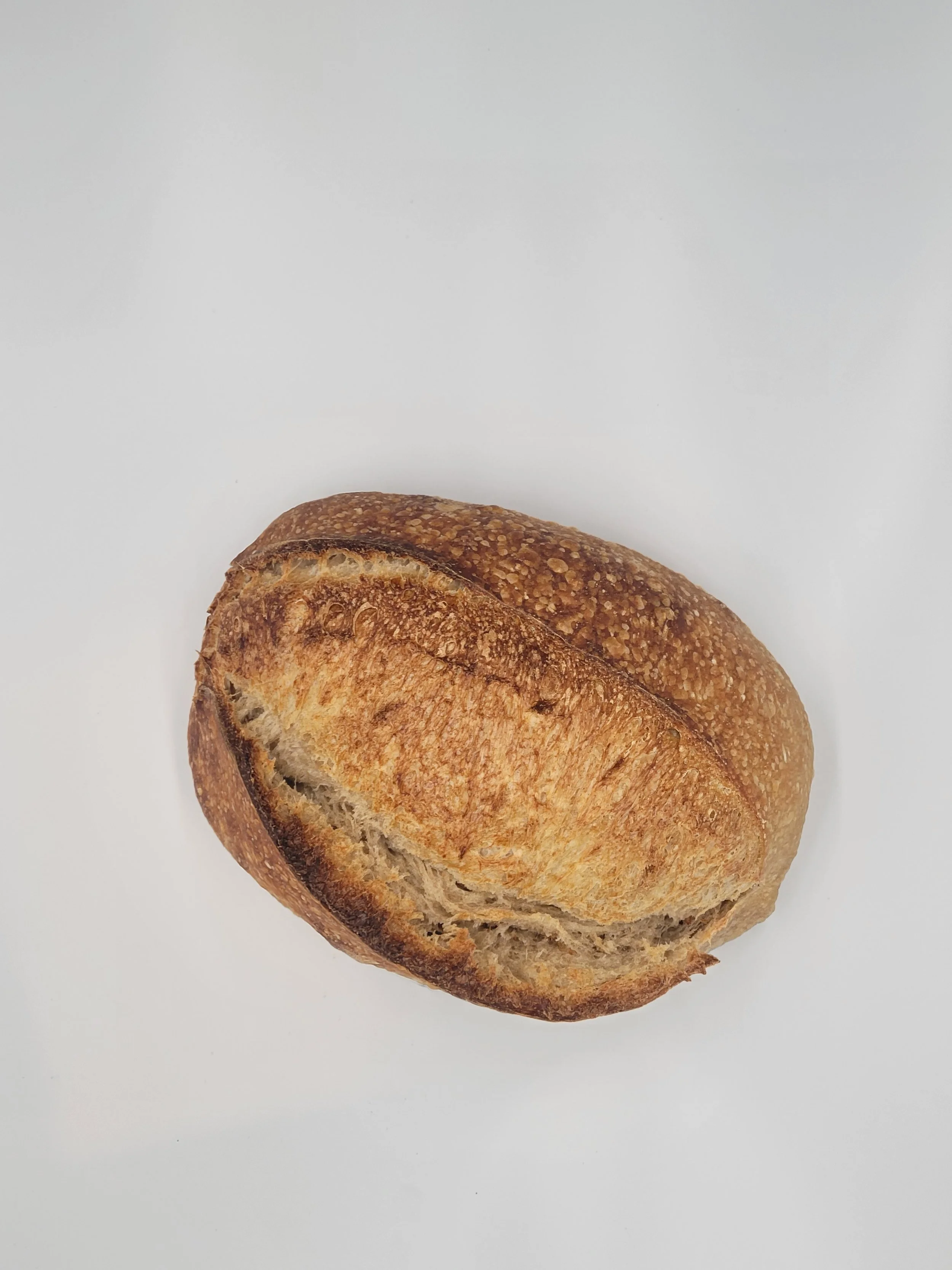 A loaf of rustic bread with a golden-brown crust on a white surface.