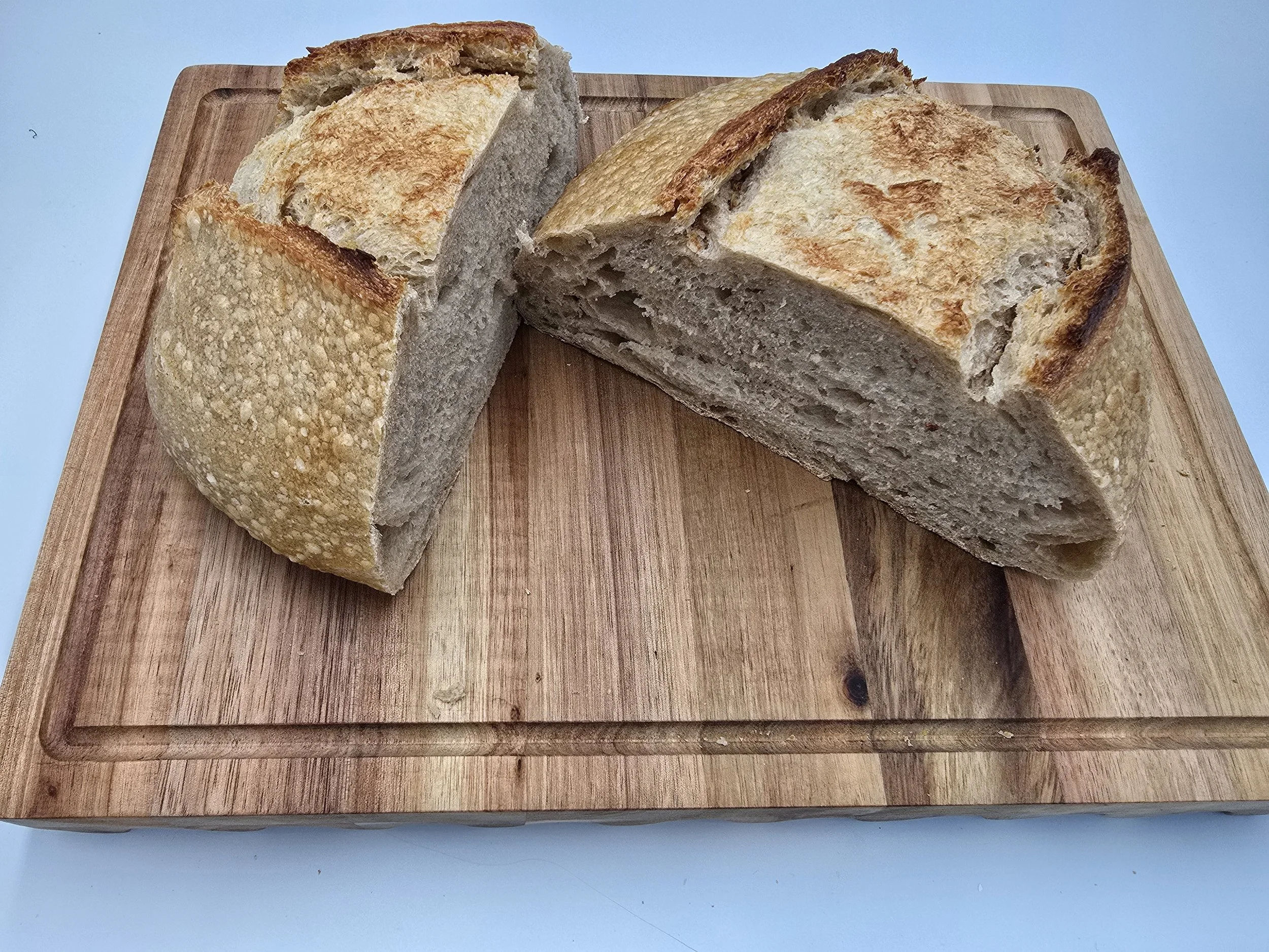 Two slices of bread on a wooden cutting board, with a crusty, round loaf.