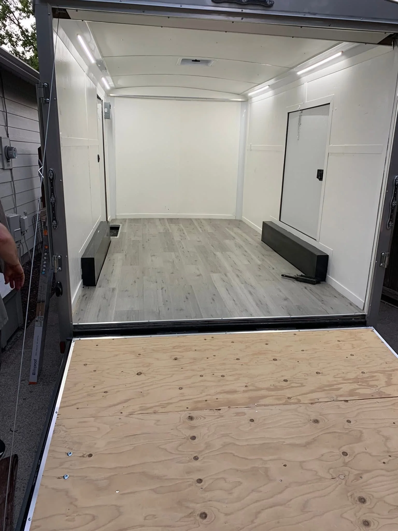 Empty cargo trailer with white interior and wood floor, with some tools and panels inside.