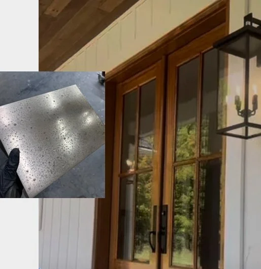 A person holding a piece of window screen with water droplets on it in front of a wooden patio door with glass panes, an outdoor lantern on the wall, and a view of greenery outside.