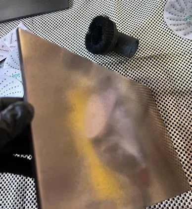 A person holding a reflective rectangular object with a black brush roll nearby on a perforated metal surface.