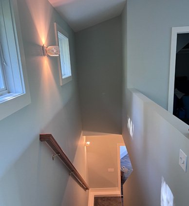 Indoor staircase with wall-mounted light, a window, and a half-wall with a door opening at the bottom.
