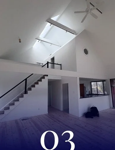 Interior of a modern, open-concept living space with a staircase, large skylights, and a ceiling fan.