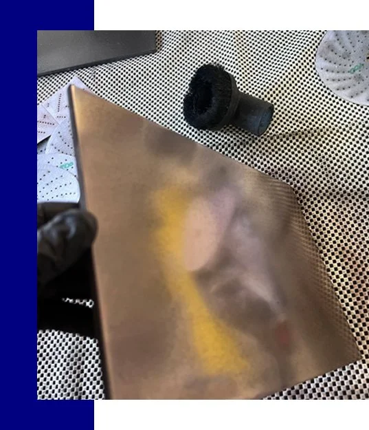 Close-up of a metal sheet on a patterned surface, with a black object and some papers nearby.