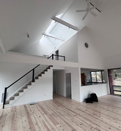 Interior of a modern, open-concept living space with a high ceiling, skylights, staircase, and large windows.